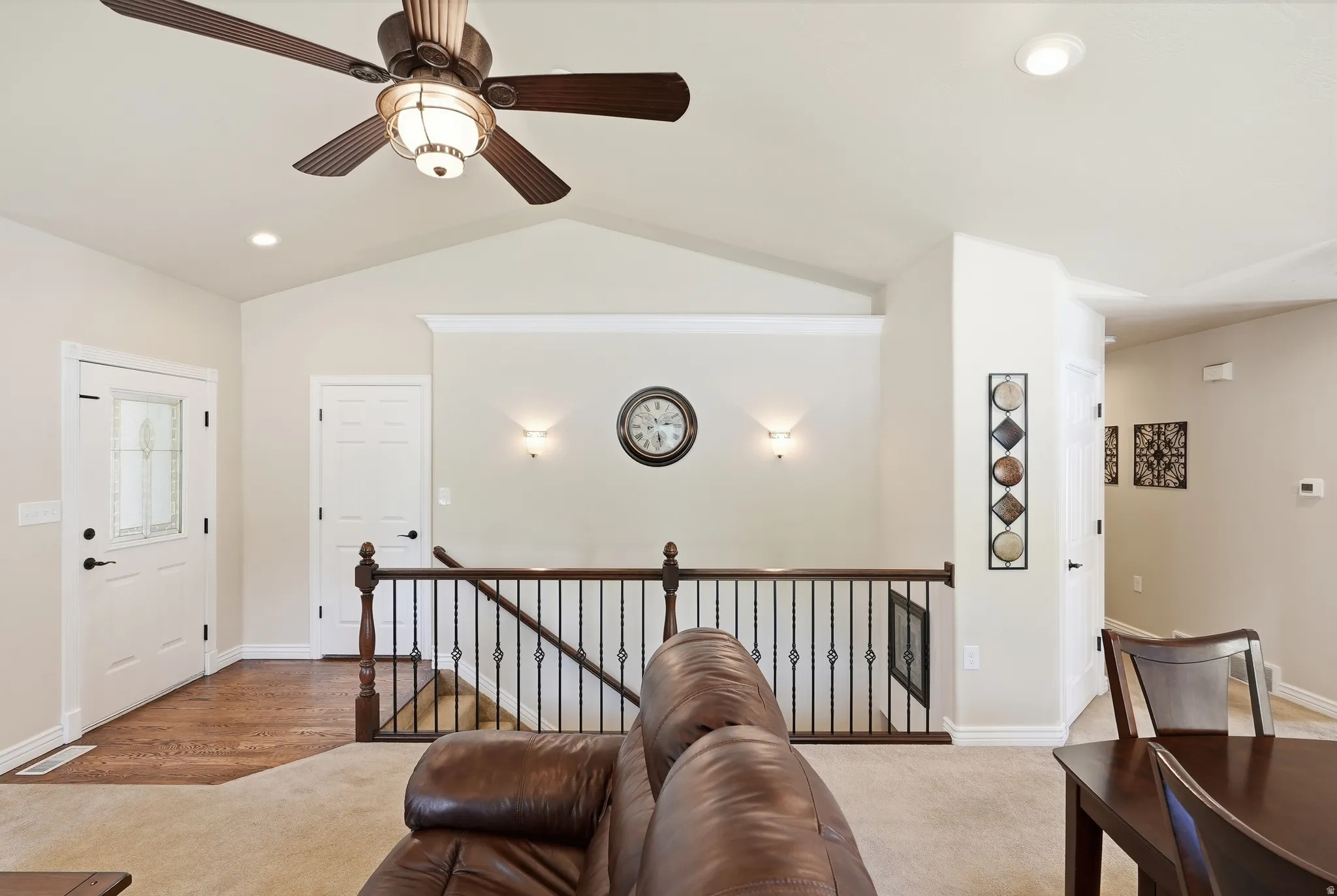 Spacious interior featuring a vaulted ceiling, ceiling fan with integrated lighting, recessed lighting, and a detailed staircase with wood railing and wrought iron spindles