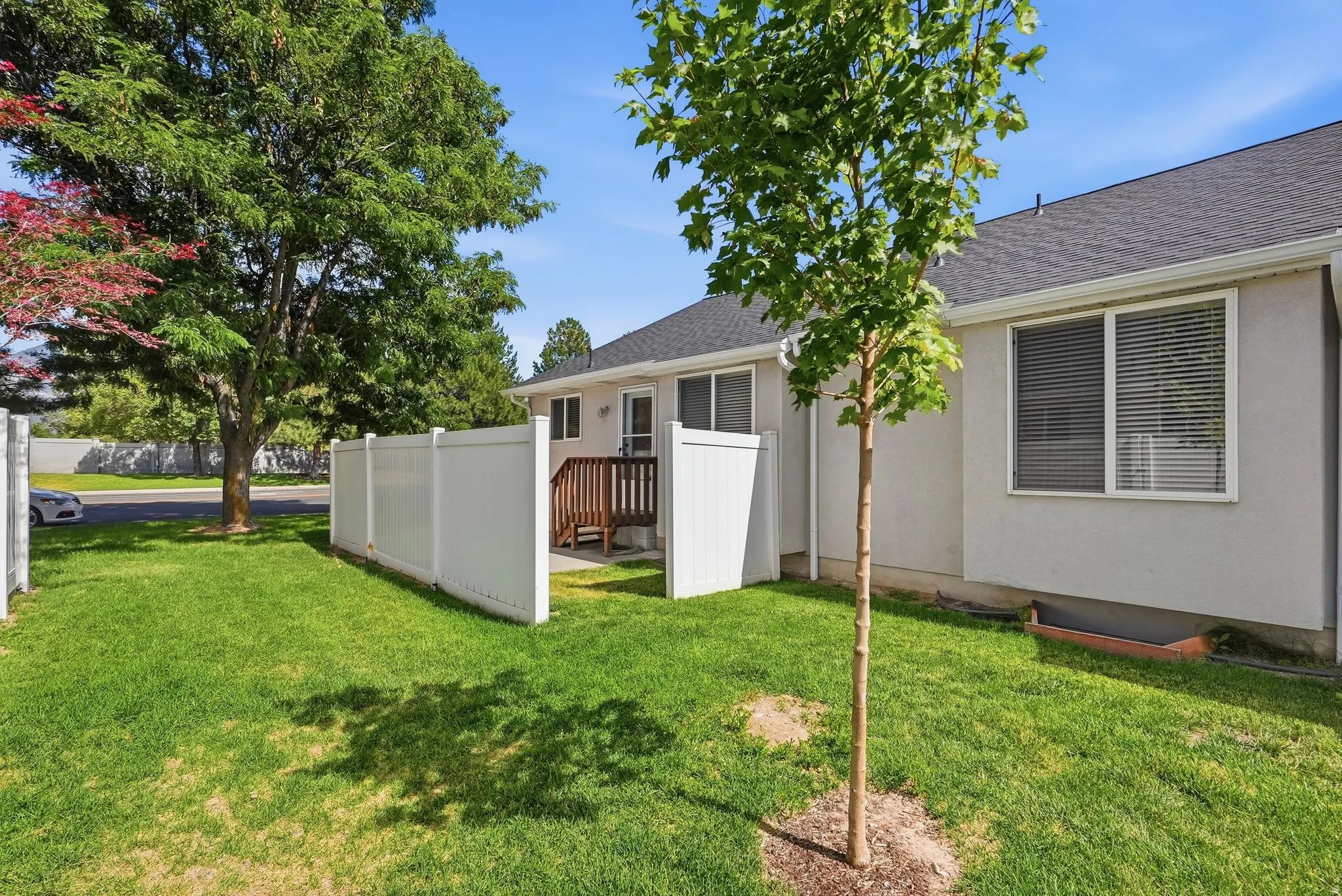 Rear exterior featuring a wood deck, white vinyl fencing, and a mature tree