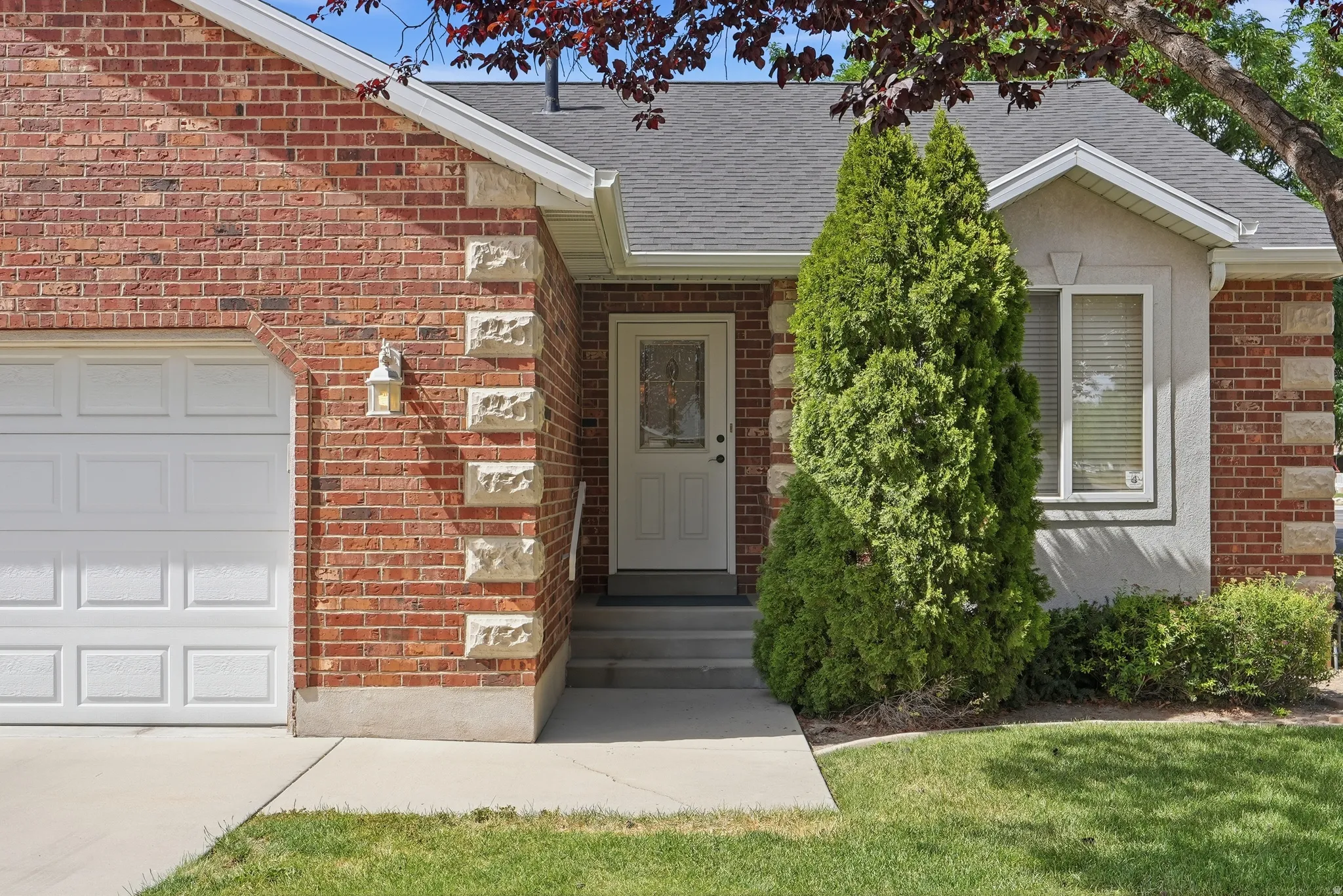 Brick and stucco exterior featuring a white paneled garage door, an arched brick detail, and a gabled roofline