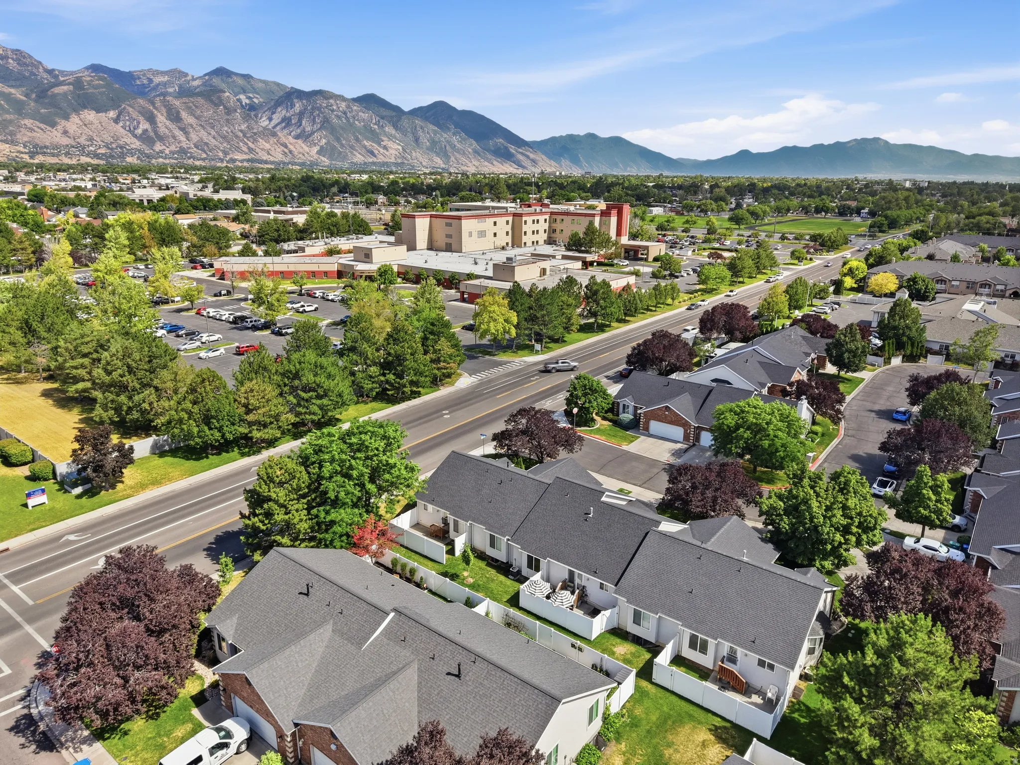 Aerial perspective showcasing residential properties with gray shingle roofs and brick facades, bordered by manicured landscaping and mature trees