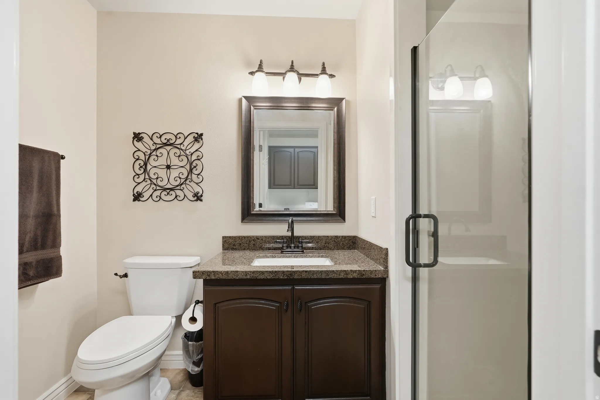 Bathroom featuring a dark wood vanity with a granite-style countertop, a framed mirror, and a three-light fixture