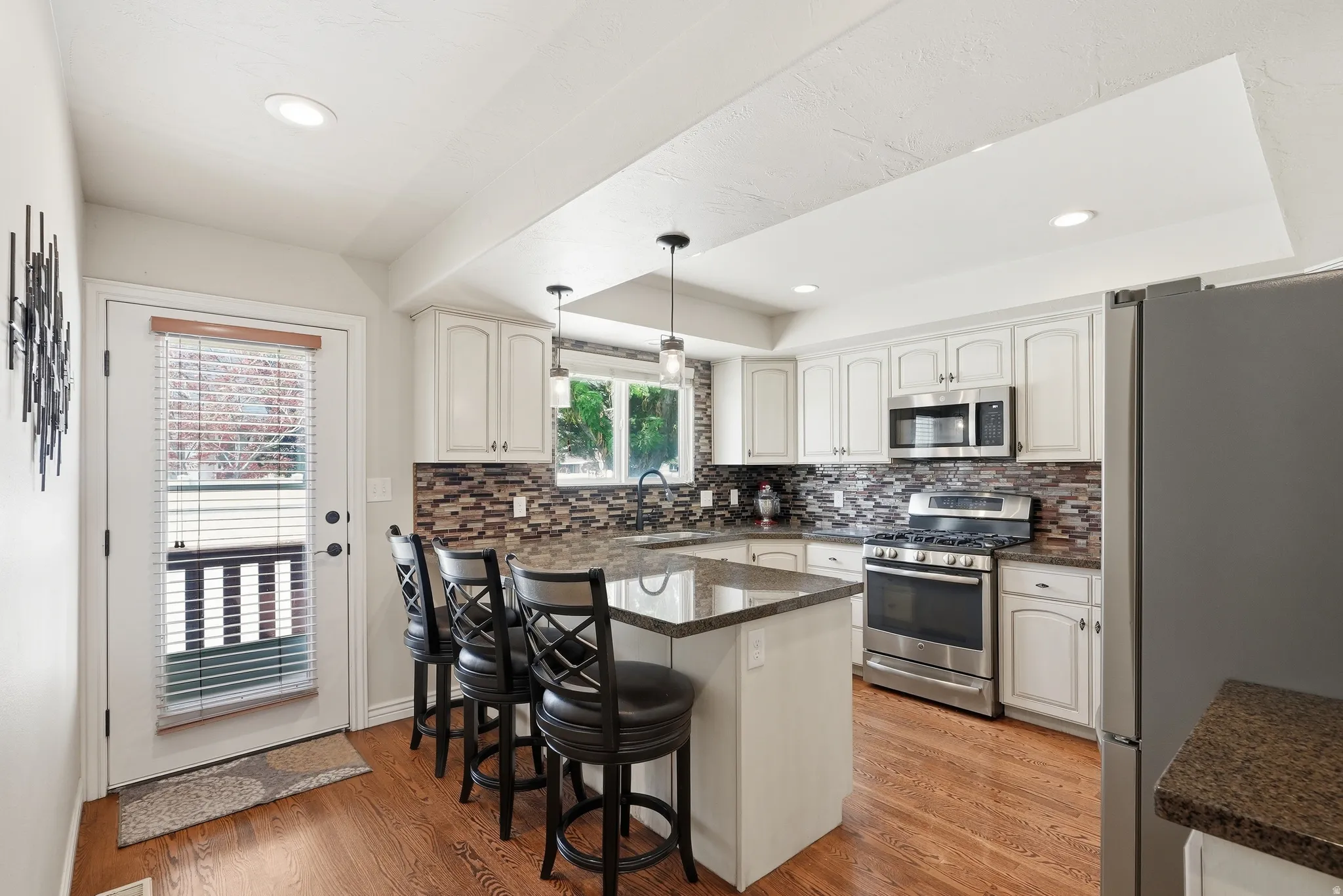 Kitchen featuring white cabinetry, stainless steel appliances, a multi-tone tile backsplash, recessed lighting, and a kitchen island with pendant lights