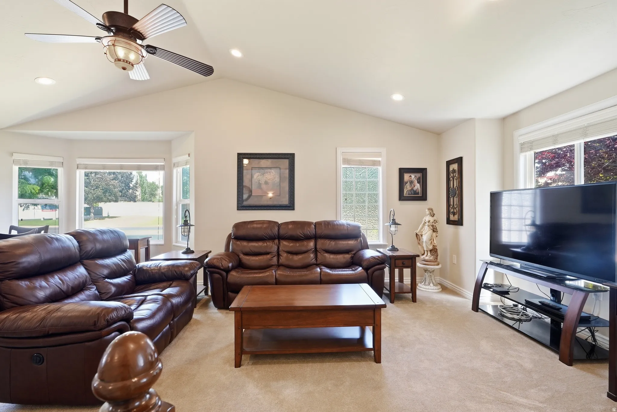 Vaulted ceiling living area featuring a ceiling fan with integrated lighting, recessed lighting, and a bay window