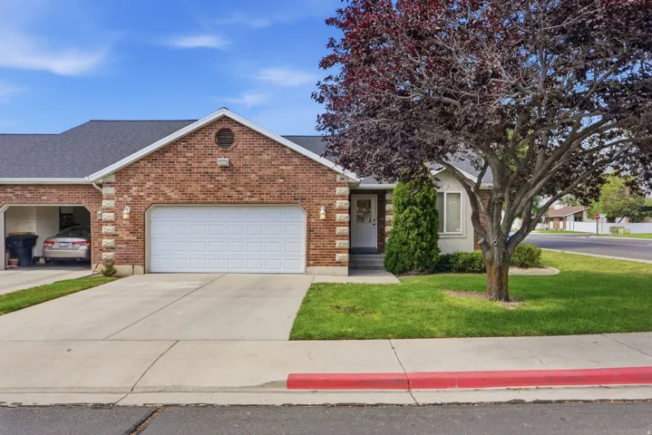 Brick exterior with a white entry door, an attached two-car garage, and a lush green lawn
