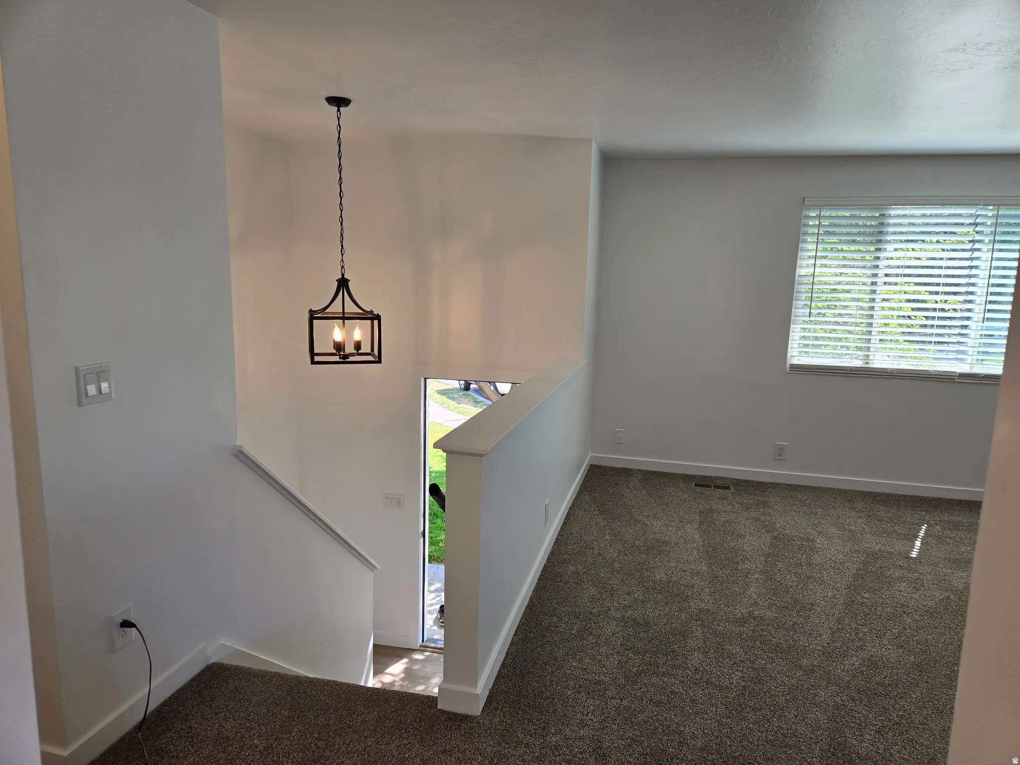 Open entryway with a modern black lantern pendant light fixture, crisp white walls, and plush grey carpeting