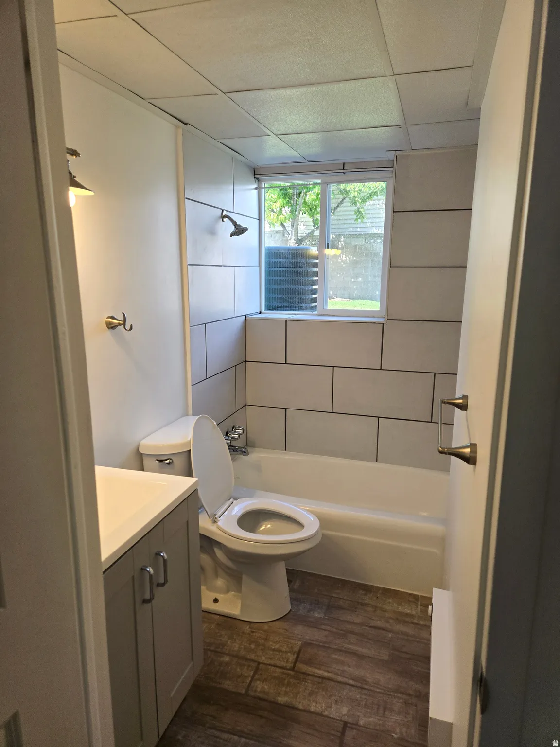 Bathroom with wood-finish flooring, white subway tile shower surround, and a white vanity with a light countertop