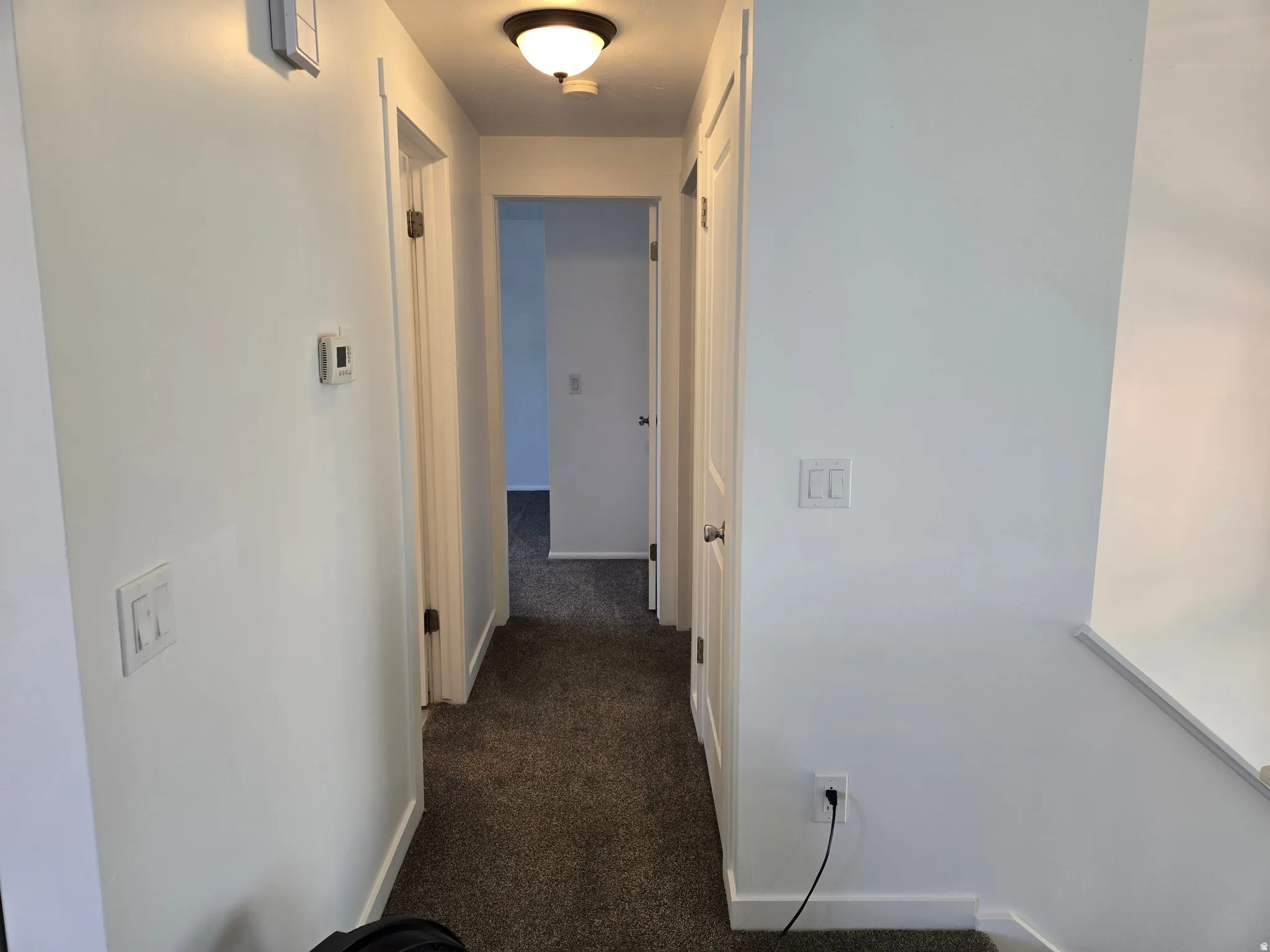 Hallway with neutral wall paint, dark carpet flooring, and white trim