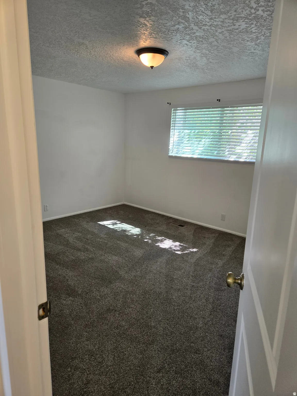 Room featuring neutral wall paint, textured ceiling, and dark patterned carpeting