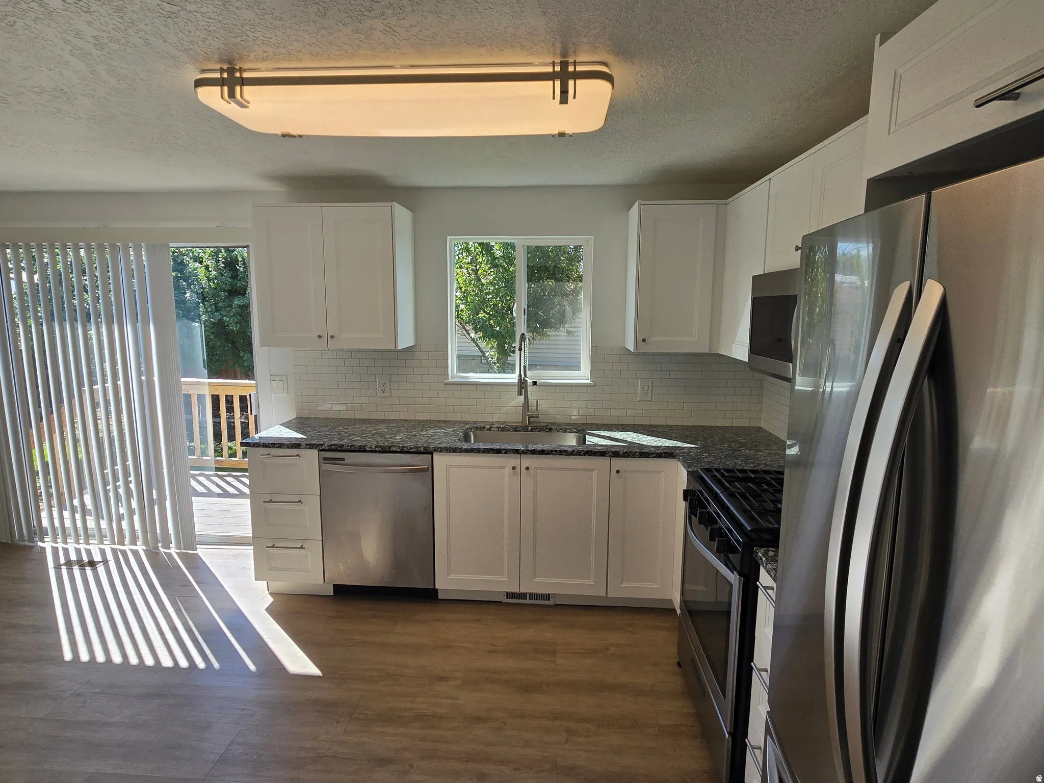 Kitchen featuring white cabinetry, stainless steel appliances, granite countertops, and a white subway tile backsplash