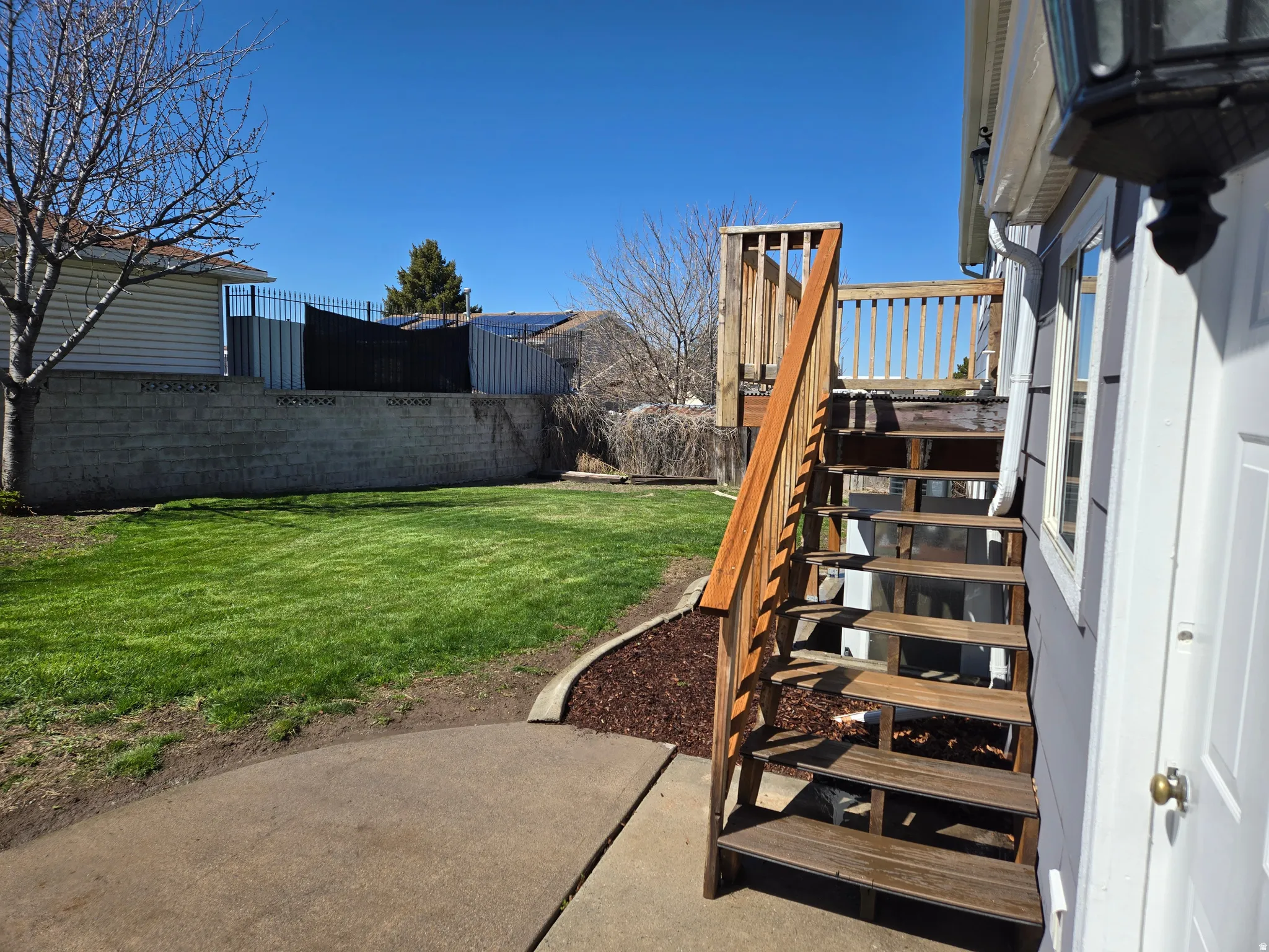Expansive green lawn with a concrete retaining wall, wood deck, and wood stairs with handrails