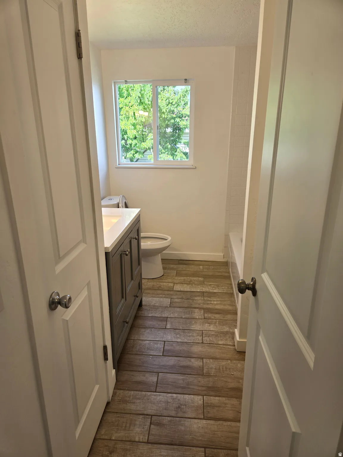 Bathroom featuring wood-finish plank flooring, a gray vanity with a white countertop, a window with natural light, and white wall tiling