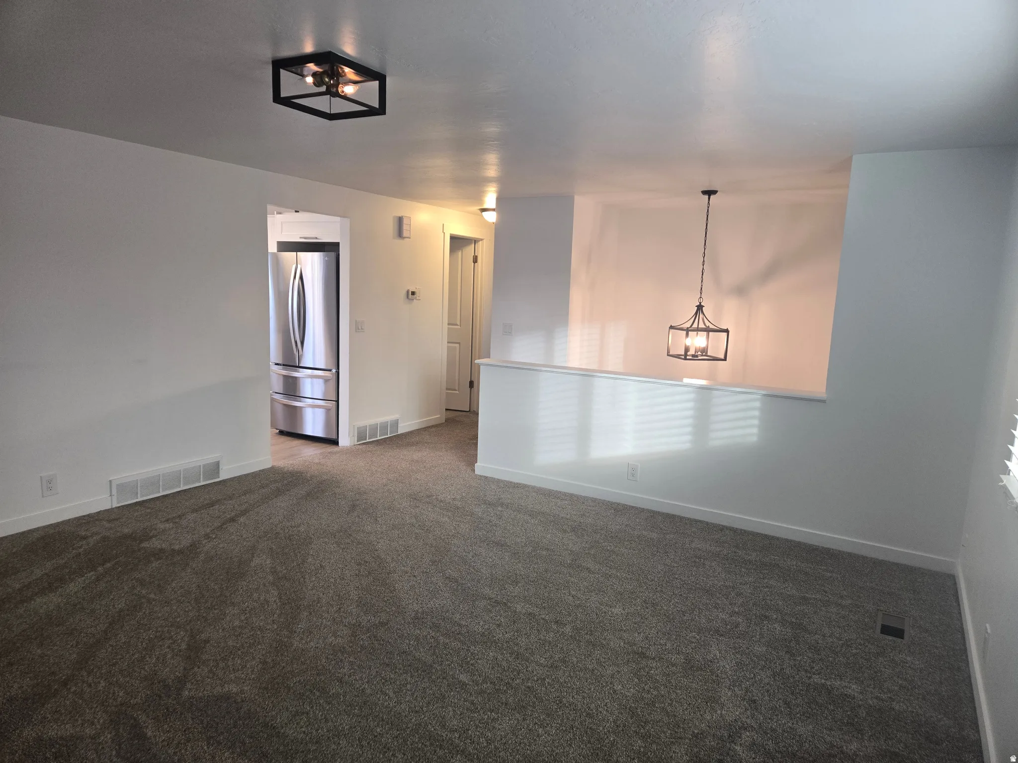 Spacious living area featuring neutral carpeting, white baseboards, and a modern flush-mount ceiling light fixture