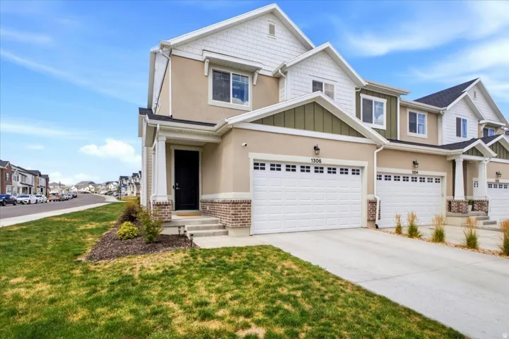 Modern townhome exterior featuring light beige stucco siding, white shaker shingles, and olive green gables