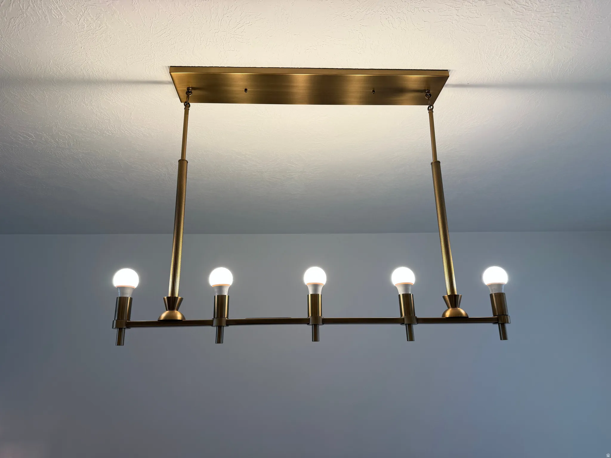 Linear chandelier with six exposed bulbs, featuring a brass finish and a rectangular ceiling mount