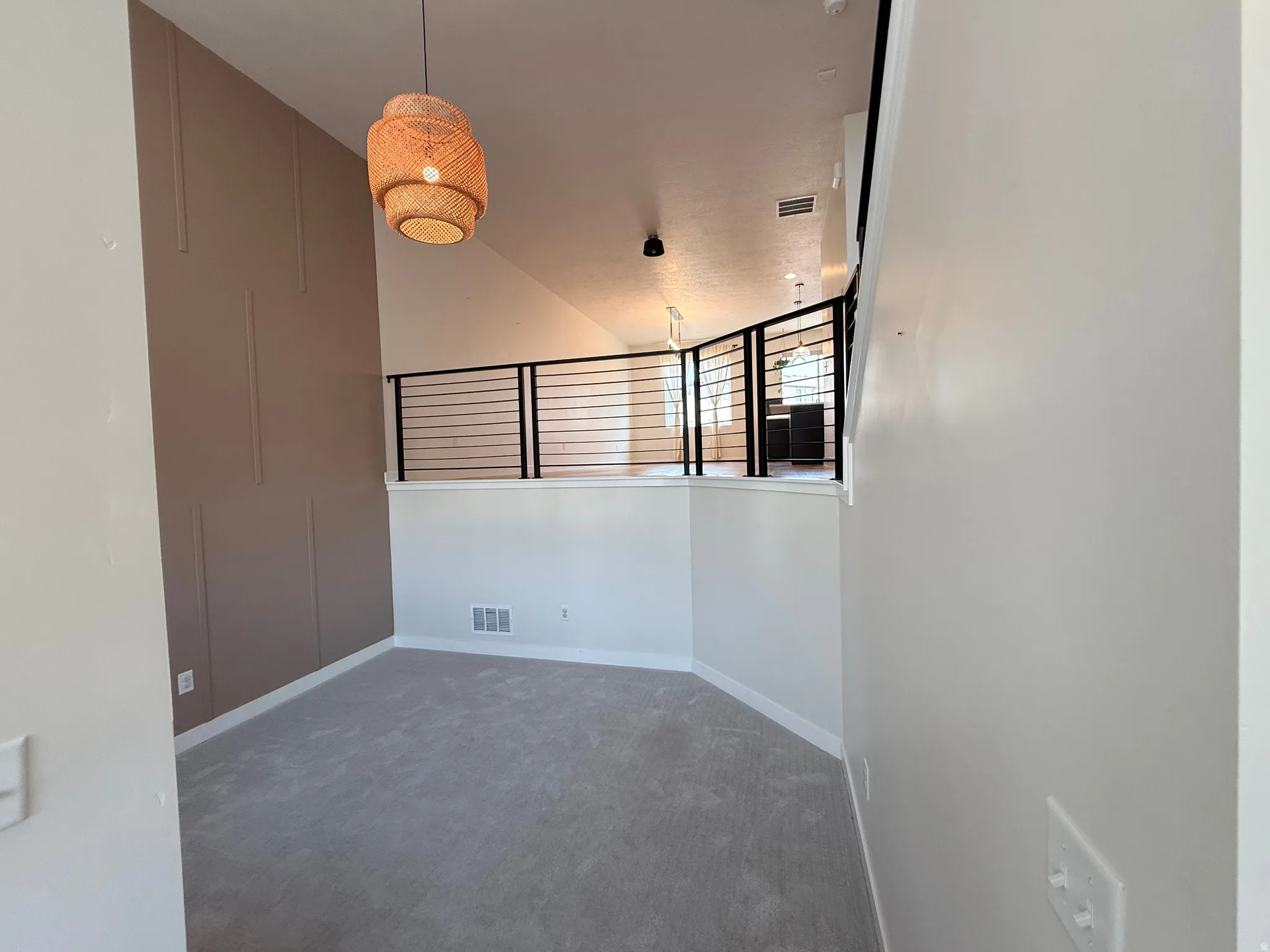 Sloped ceiling featuring a decorative pendant light fixture, loft area with metal horizontal railing, light gray carpeting, and an accent wall