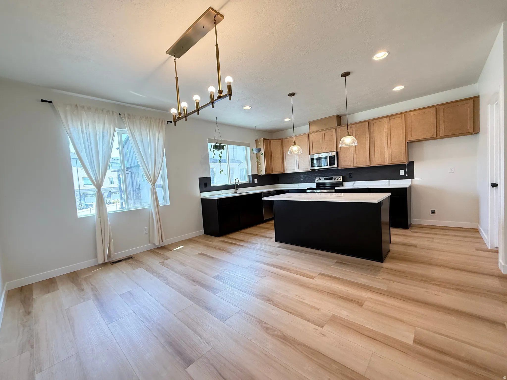 Bright open-concept kitchen and dining area featuring wood-finish flooring, a kitchen island with a light-colored countertop, and a tiled backsplash