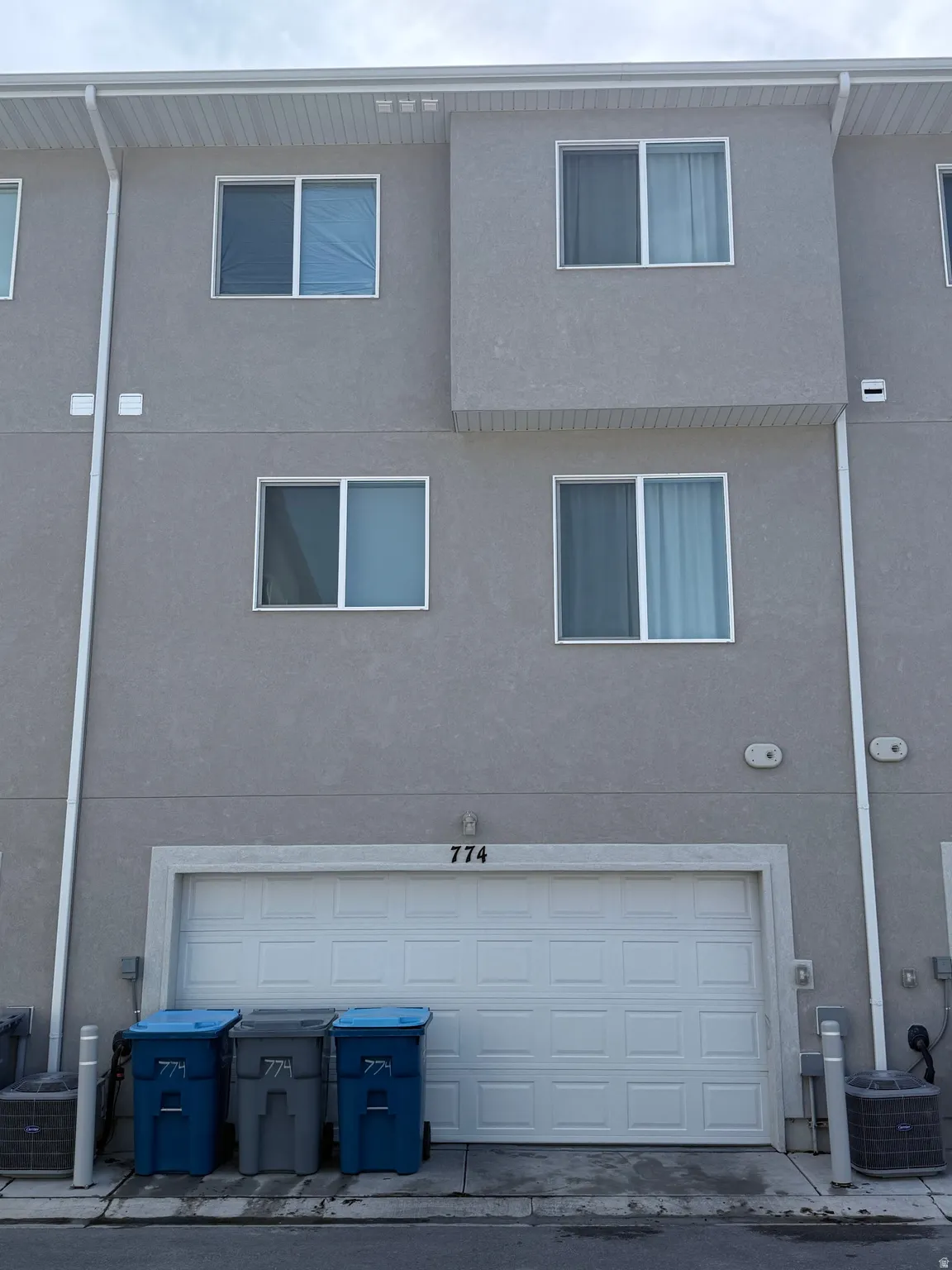 Multi-story stucco exterior with white window frames and a two-car garage