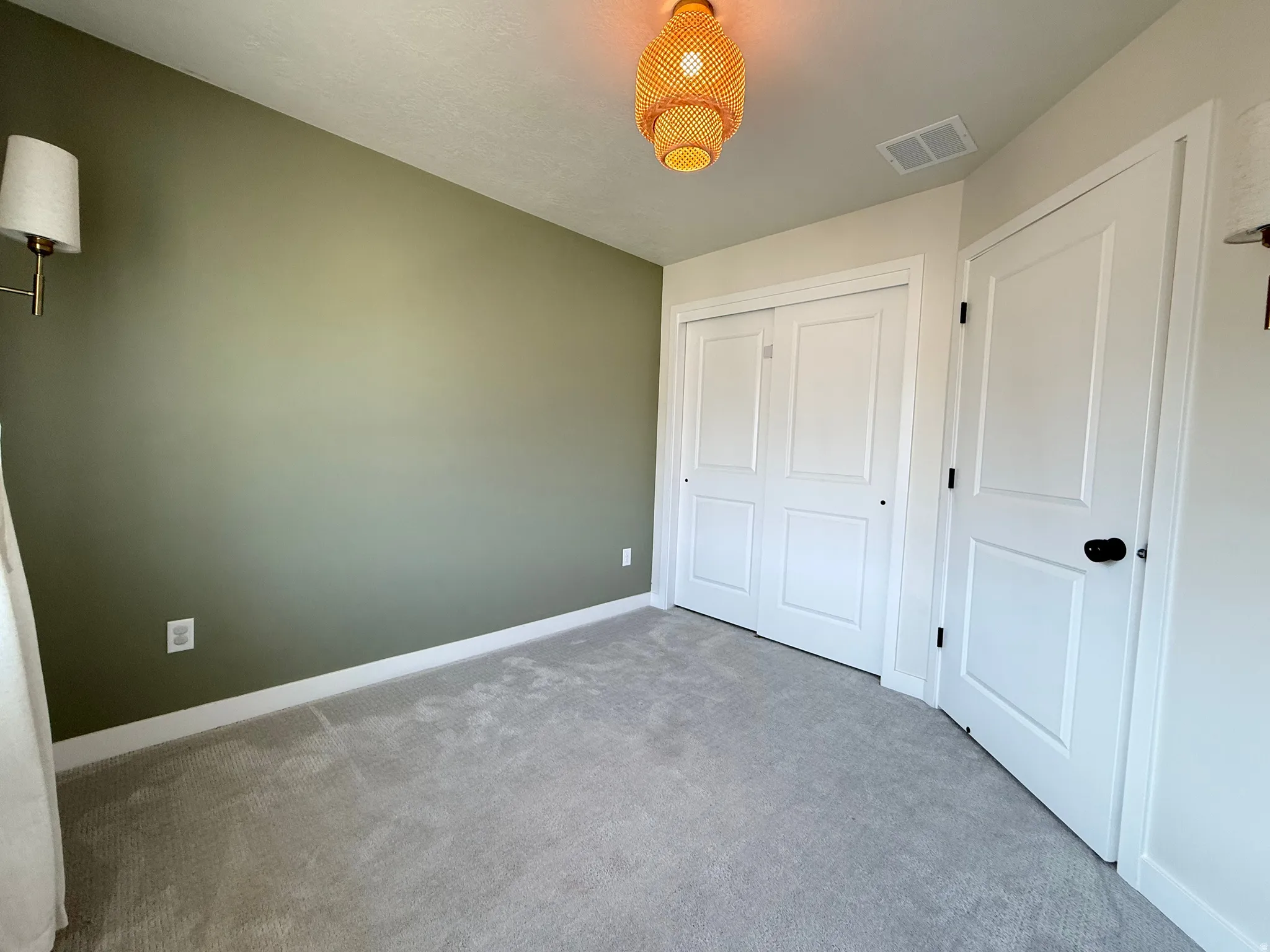 Carpeted room featuring a ceiling-mounted light fixture, wall sconces, and built-in closet with bi-fold doors