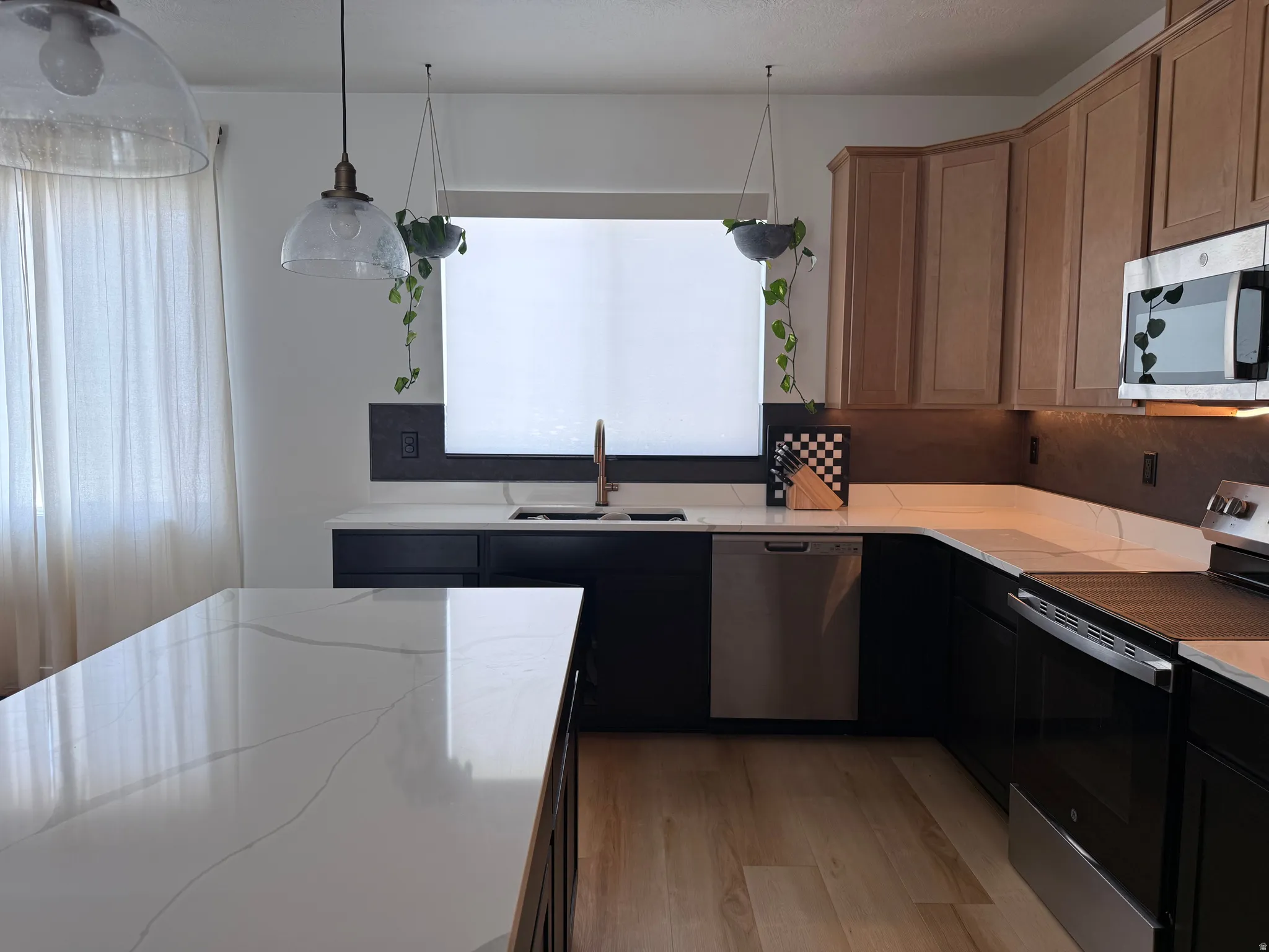 Kitchen featuring an expansive island with a white countertop, coordinating perimeter countertops, light wood-finish flooring, and a mix of black and natural wood cabinetry