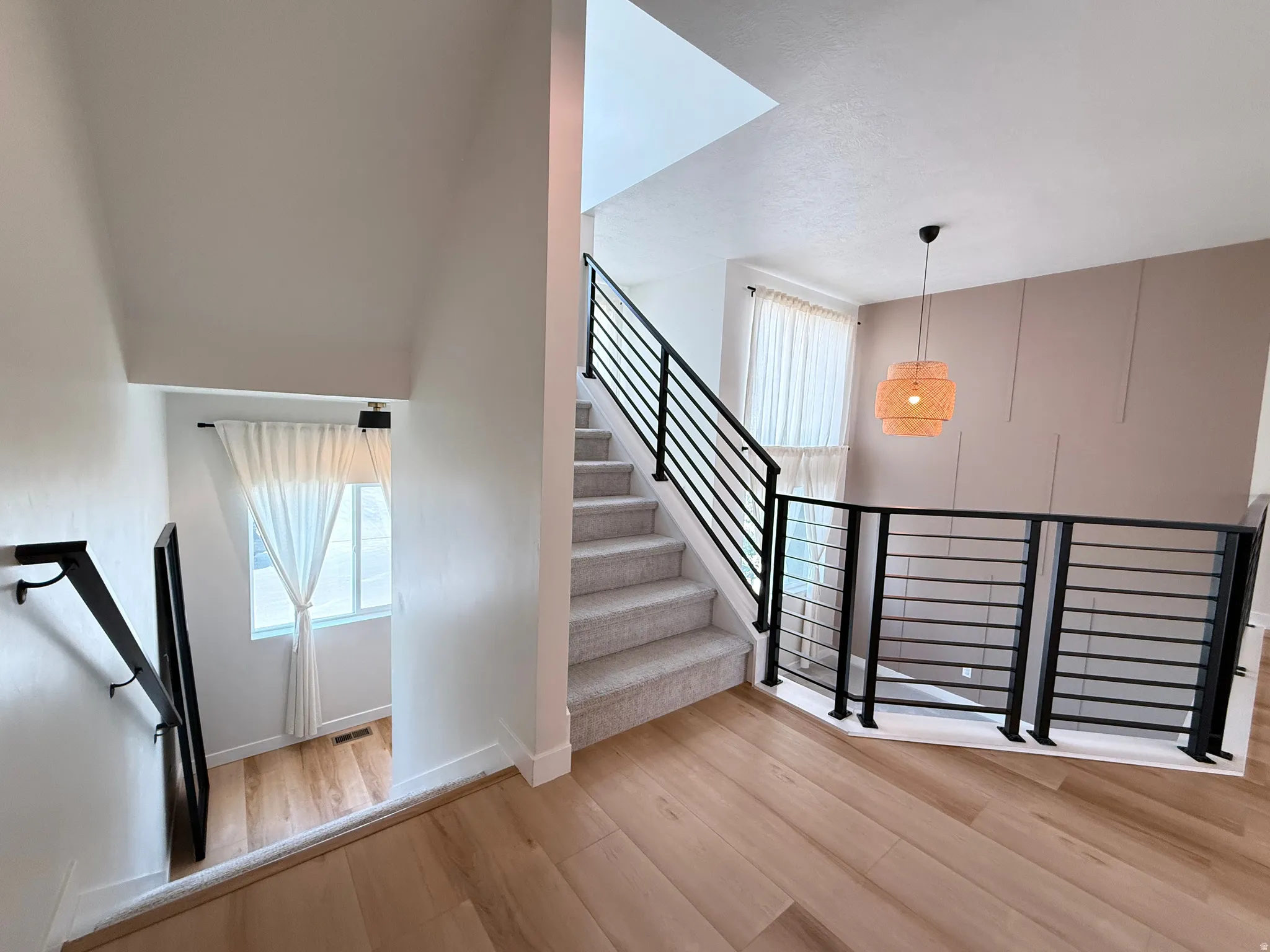 Carpeted staircase with black metal railings, wood-finish flooring, and a decorative wall panel