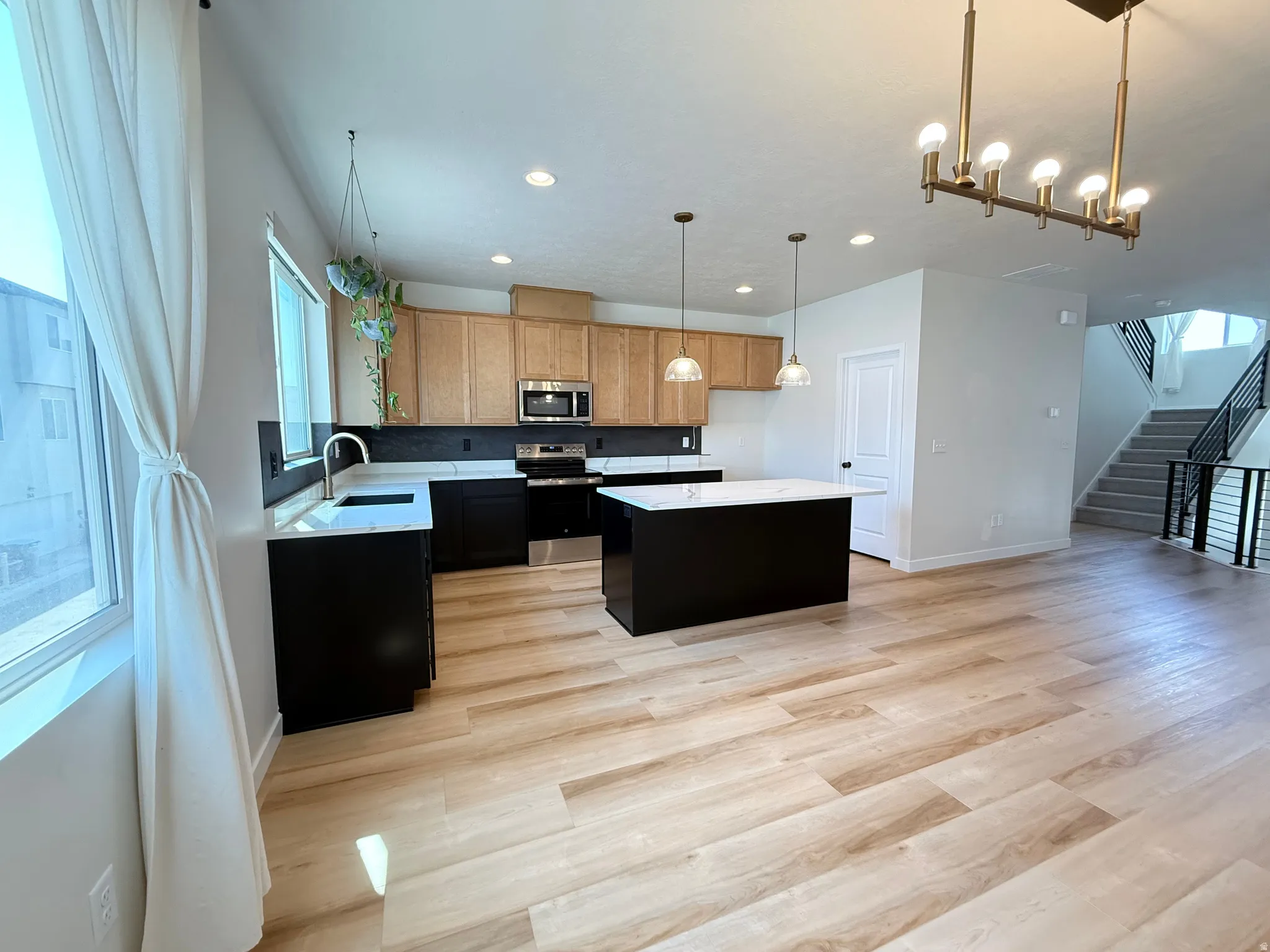 Open-concept kitchen featuring wood-finish flooring, a central island with a white countertop, and stainless steel appliances