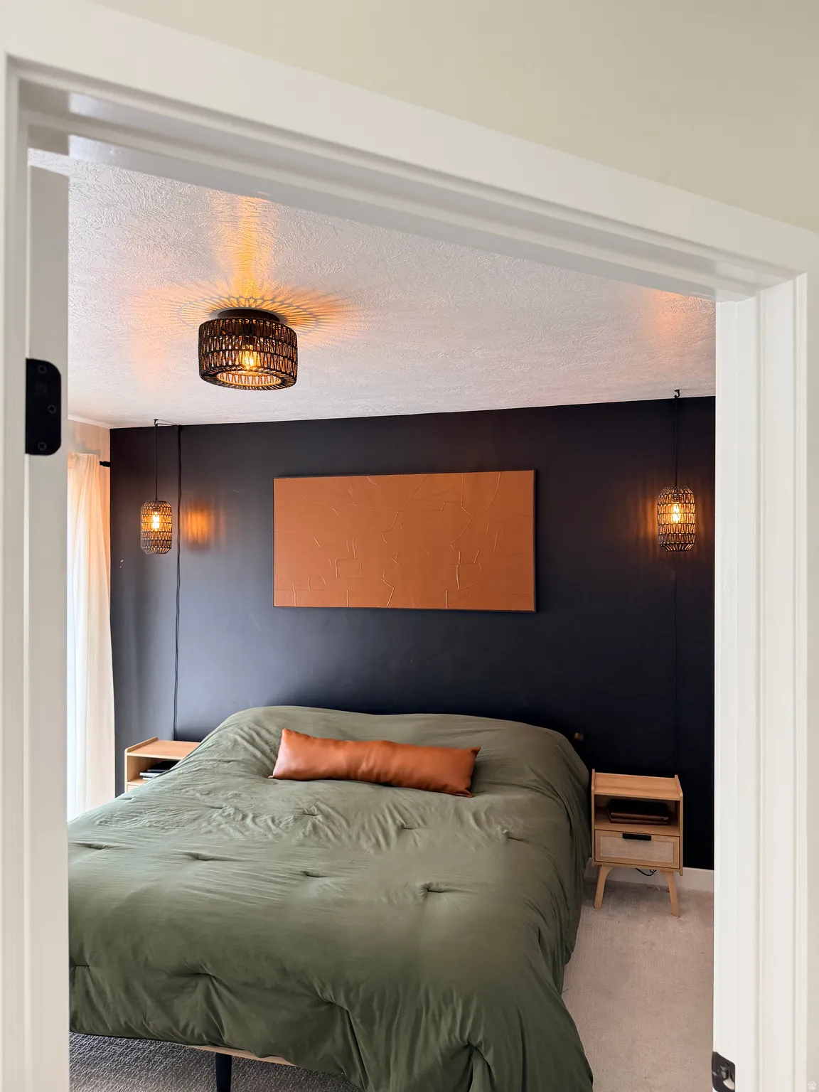 Carpeted room featuring a dark accent wall with a wall-mounted art piece, a flush-mount ceiling light fixture, and two pendant light fixtures