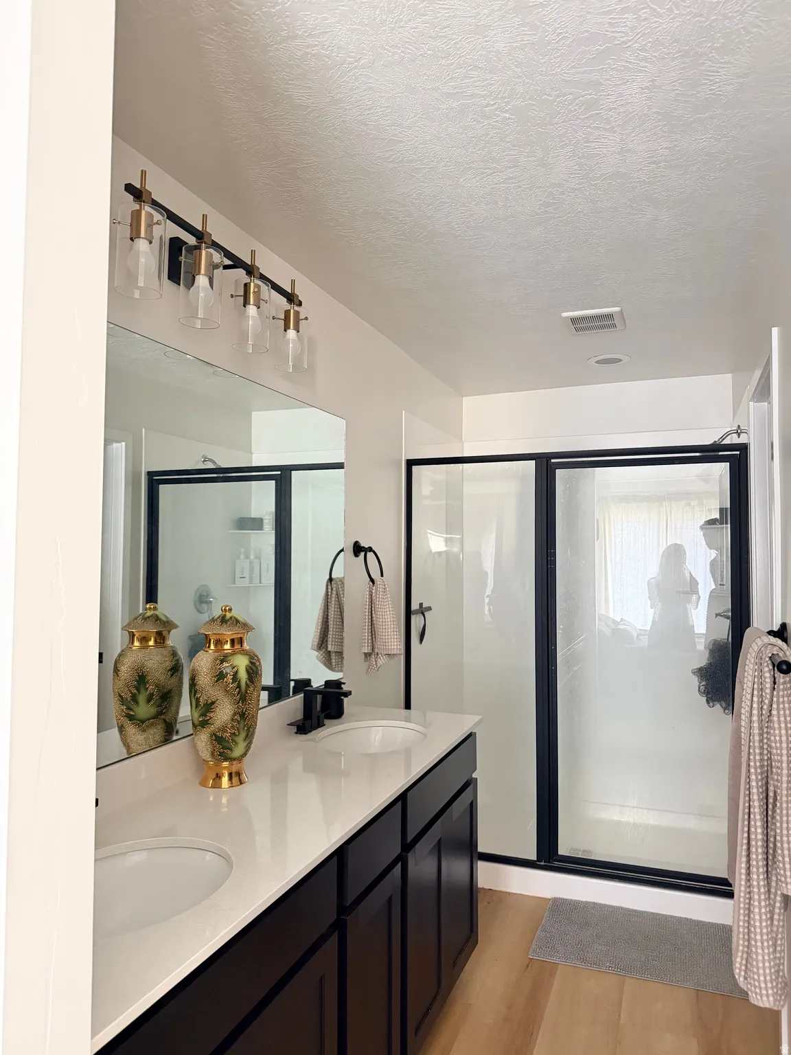 Bathroom featuring a dual vanity with dark wood cabinetry and white countertops, matte black faucets, and a large frameless mirror