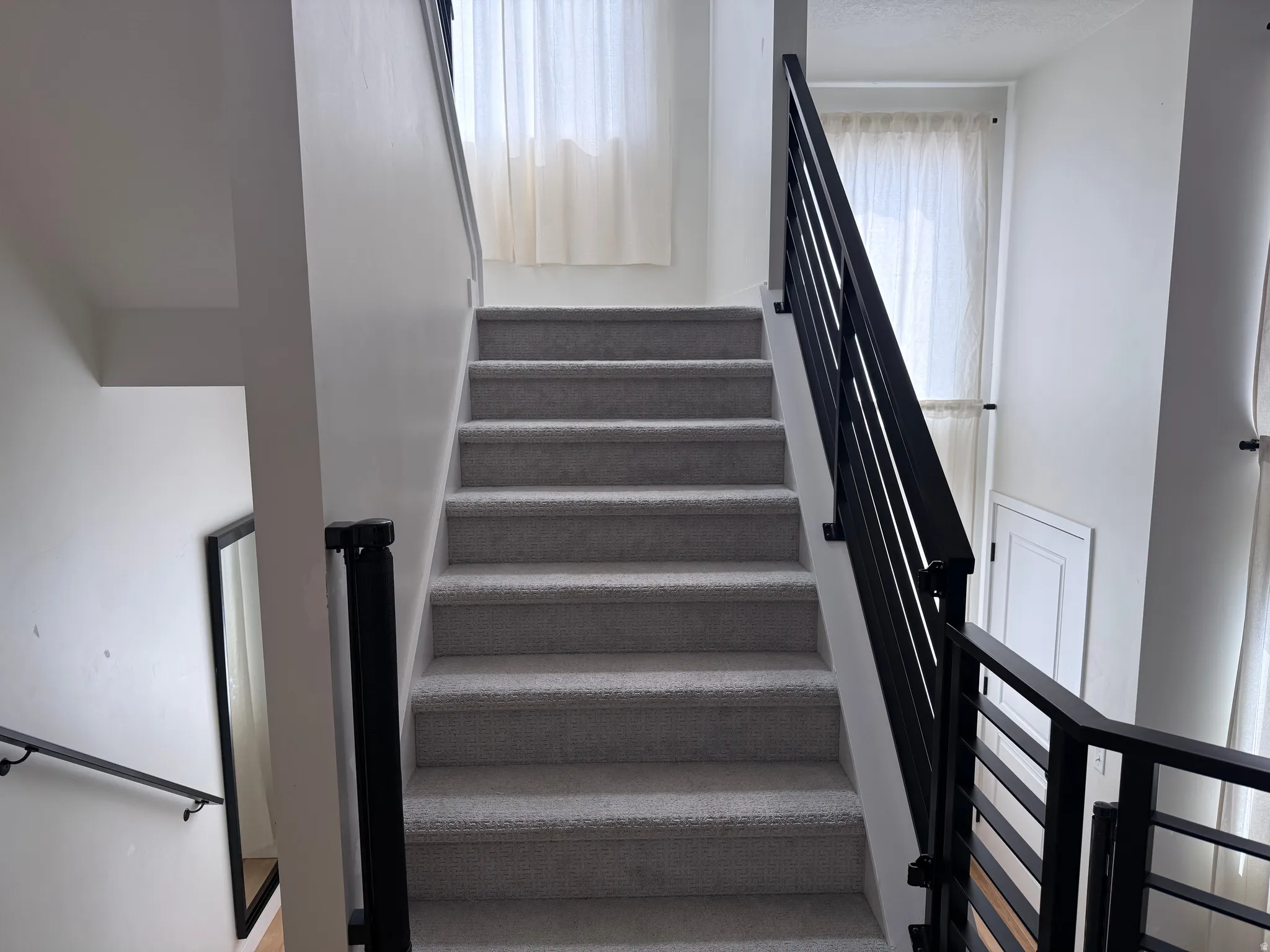 Staircase featuring light gray carpeting and black metal railings with horizontal spindles