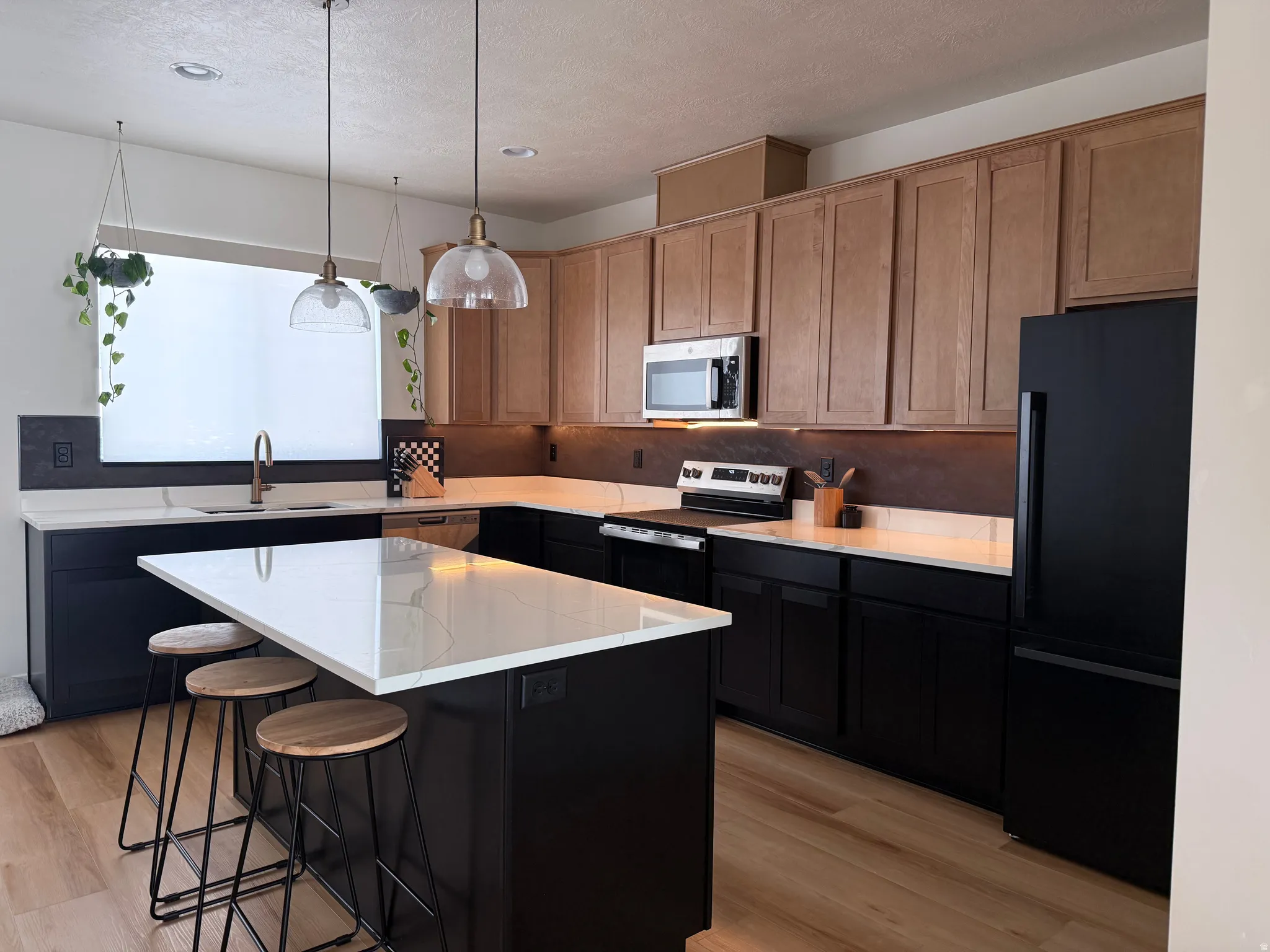 Modern kitchen featuring a large island with a light-colored countertop, dark lower cabinetry, and complementary wood-finish upper cabinetry