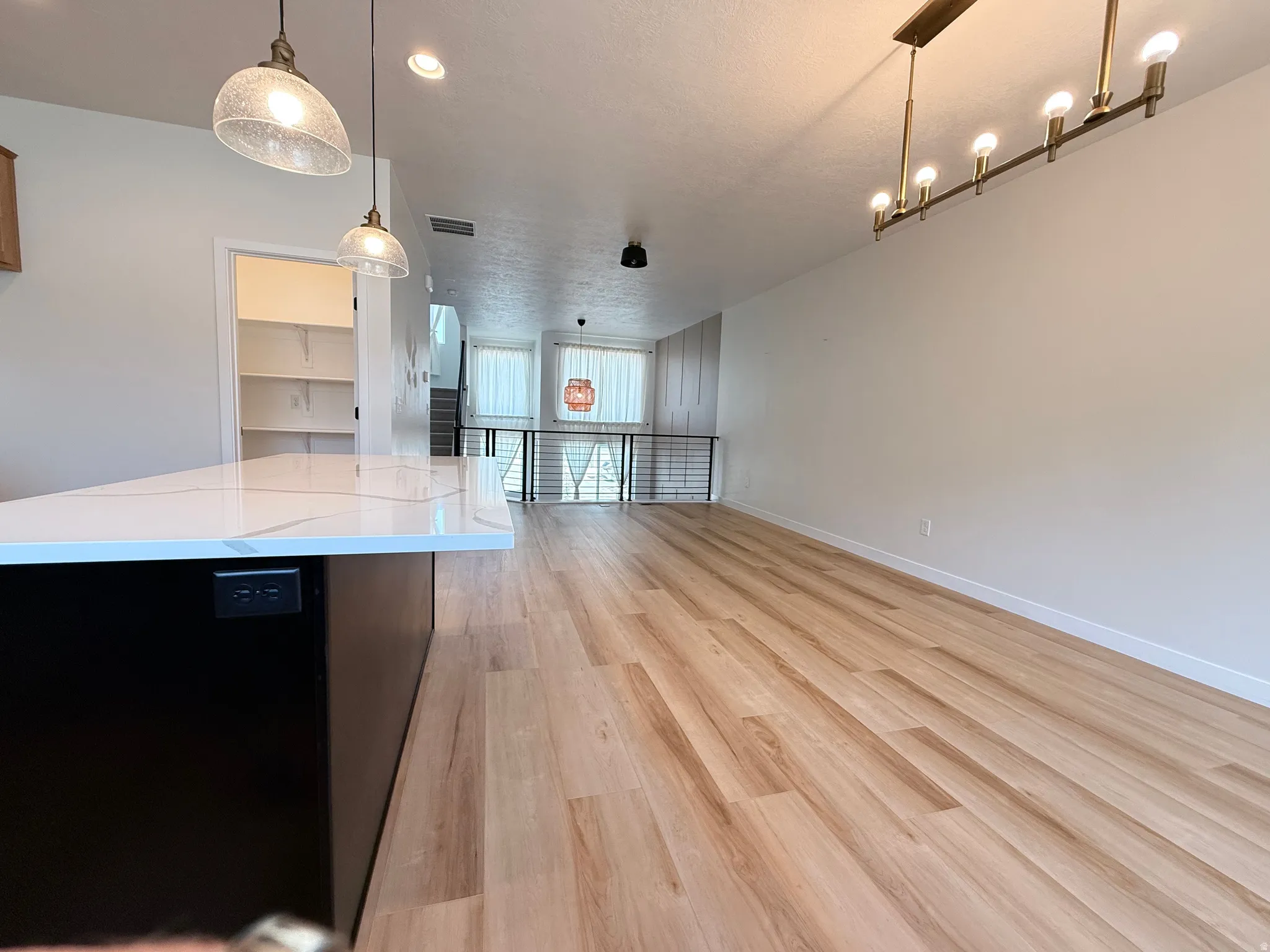 Open-concept living area with wood-finish flooring, a contemporary linear chandelier, and a kitchen island featuring a white countertop