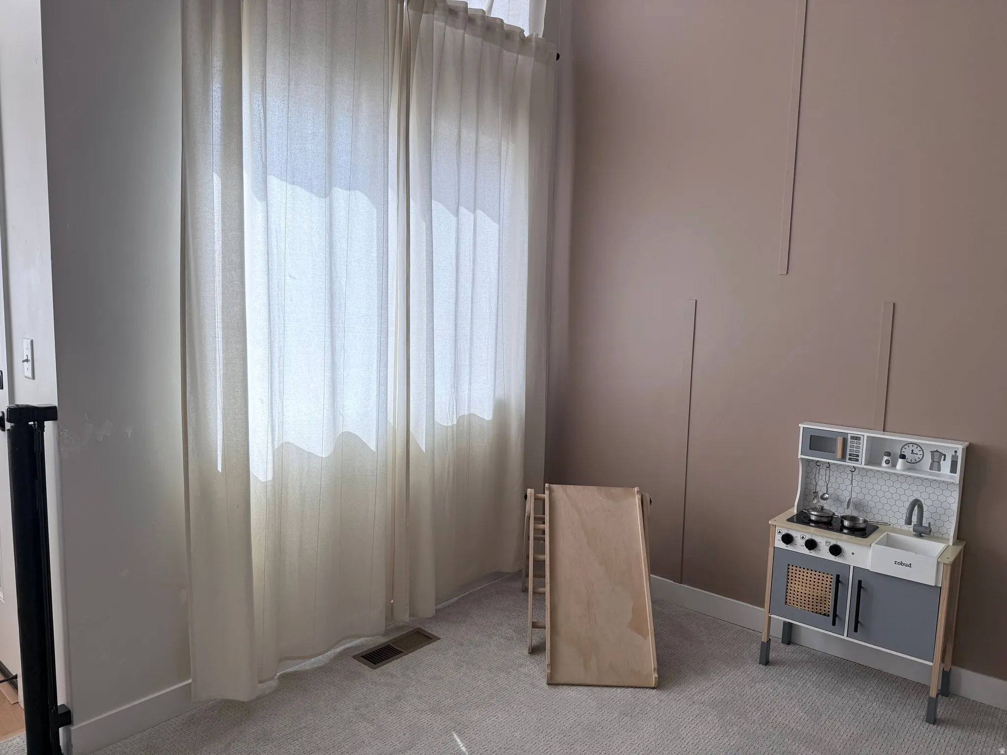 Room featuring plush carpet flooring, a large window with full-length draperies, an accent wall with vertical paneling, and neutral-toned paint finishes