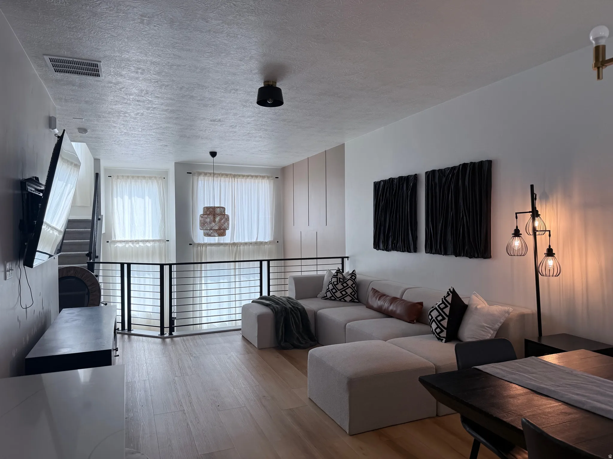 Open-concept living space featuring wood-finish flooring, a contemporary railing system, and large windows with privacy blinds