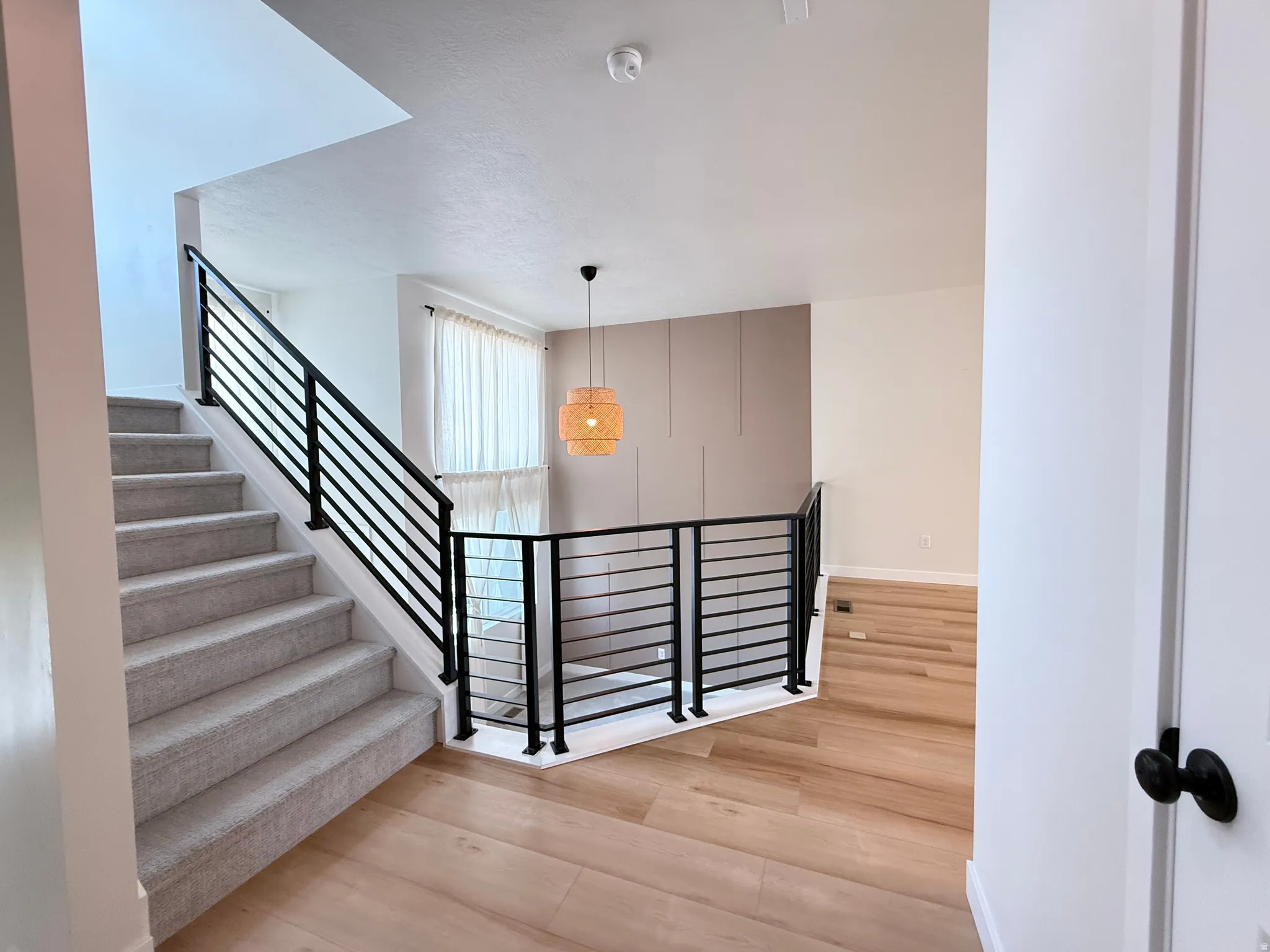 Hardwood-style flooring in common areas, carpeted staircase with modern black iron railings, and a contemporary hanging light fixture