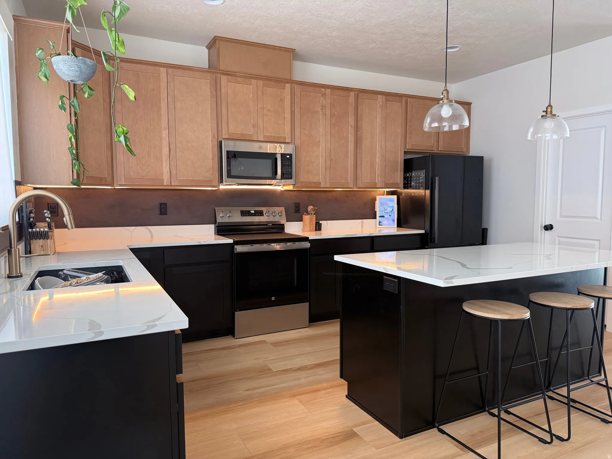 Modern kitchen featuring a large central island, light wood-finish flooring, and white countertops with dark veining