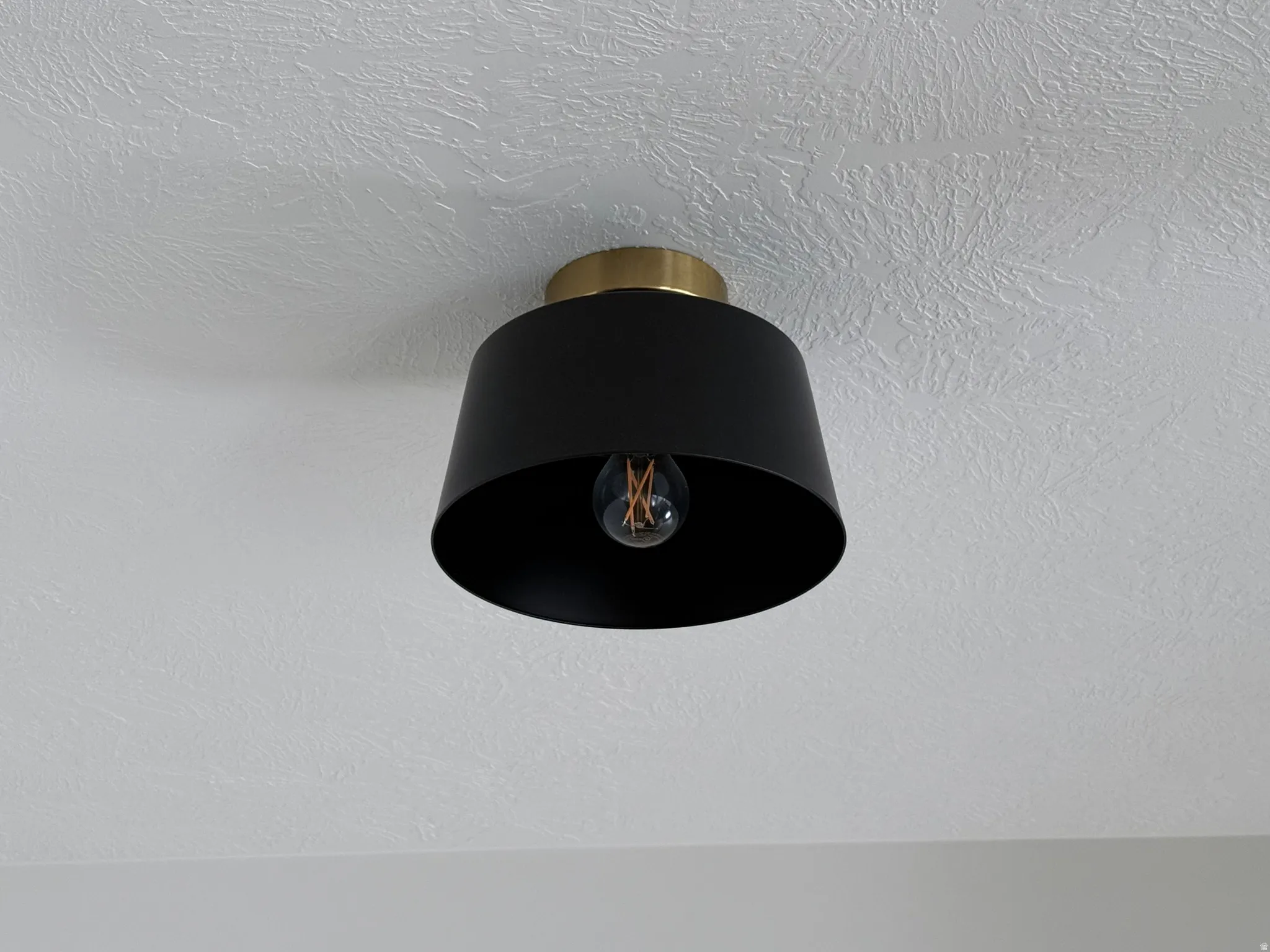 Contemporary flush-mount light fixture with a matte black shade and brass-tone base