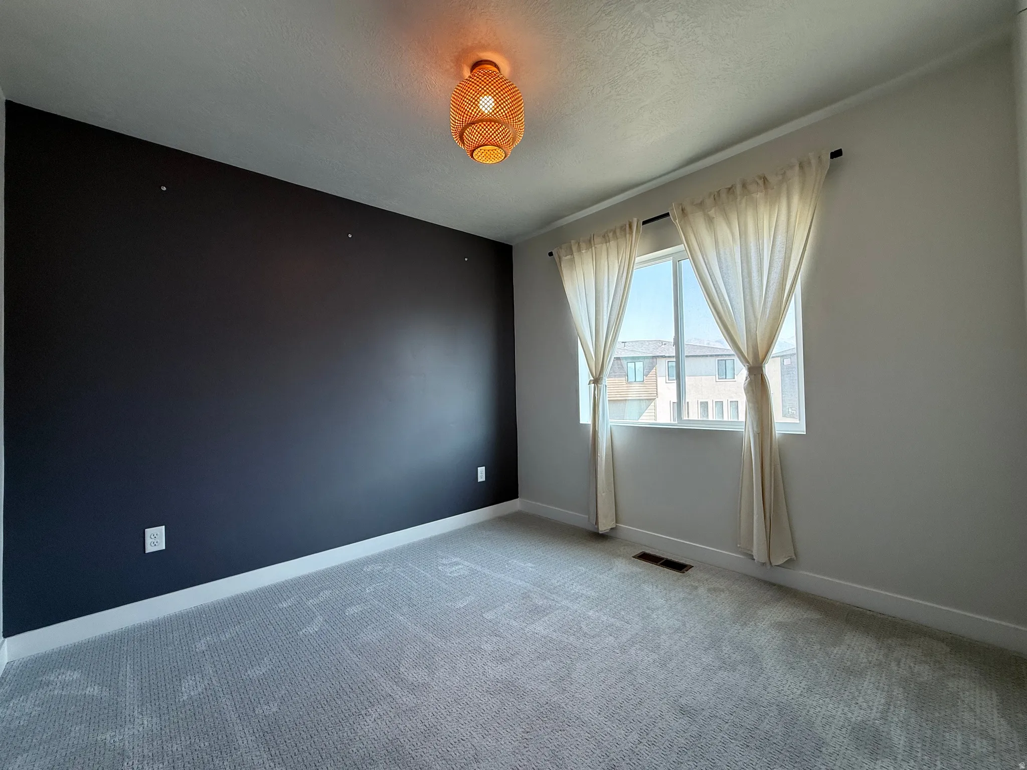 Dark accent wall, textured gray carpet, single window with light-colored drapes, contemporary ceiling light fixture