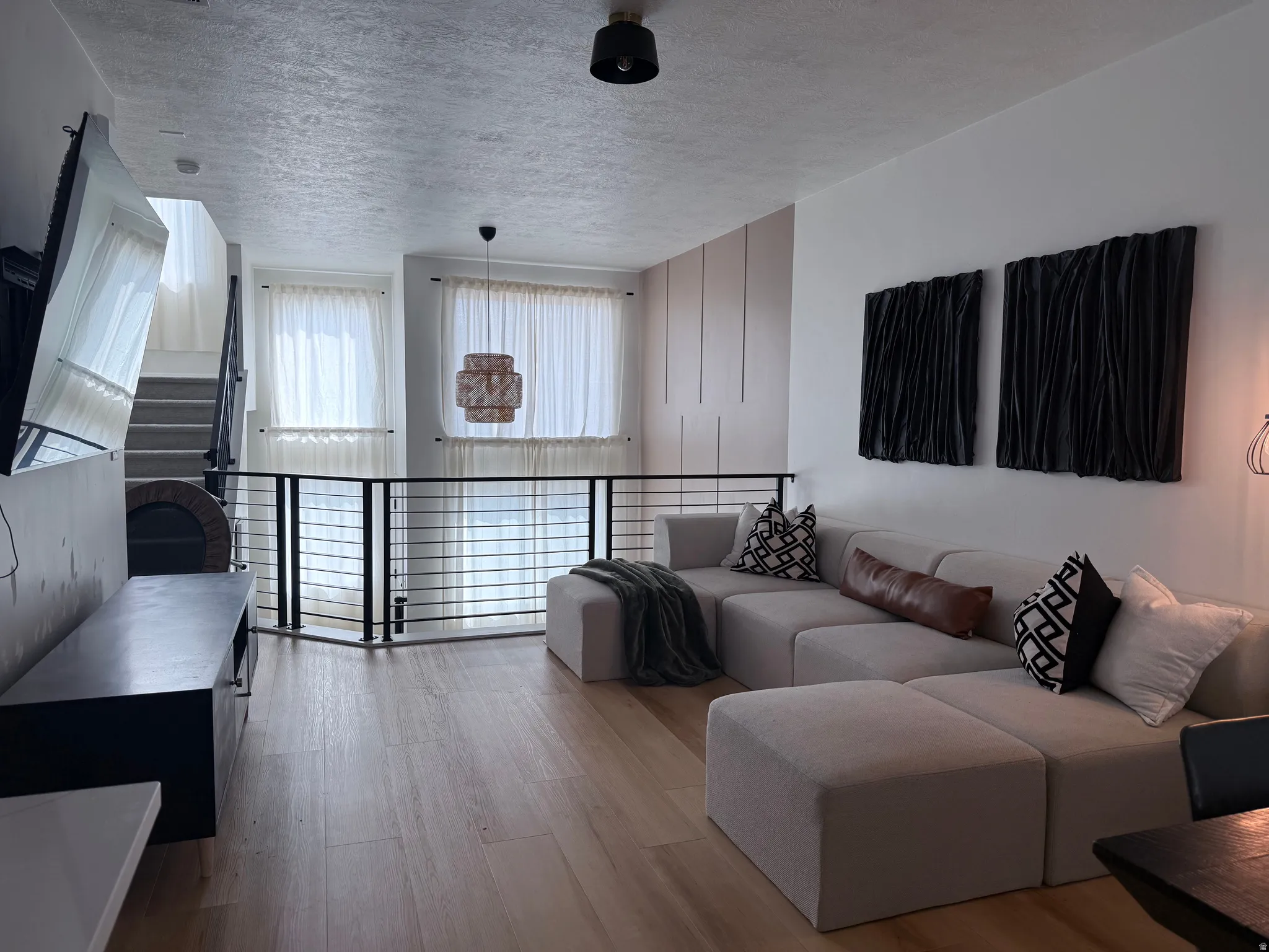 Open-concept living space featuring wood-finish flooring, a contemporary black metal railing, and high ceilings