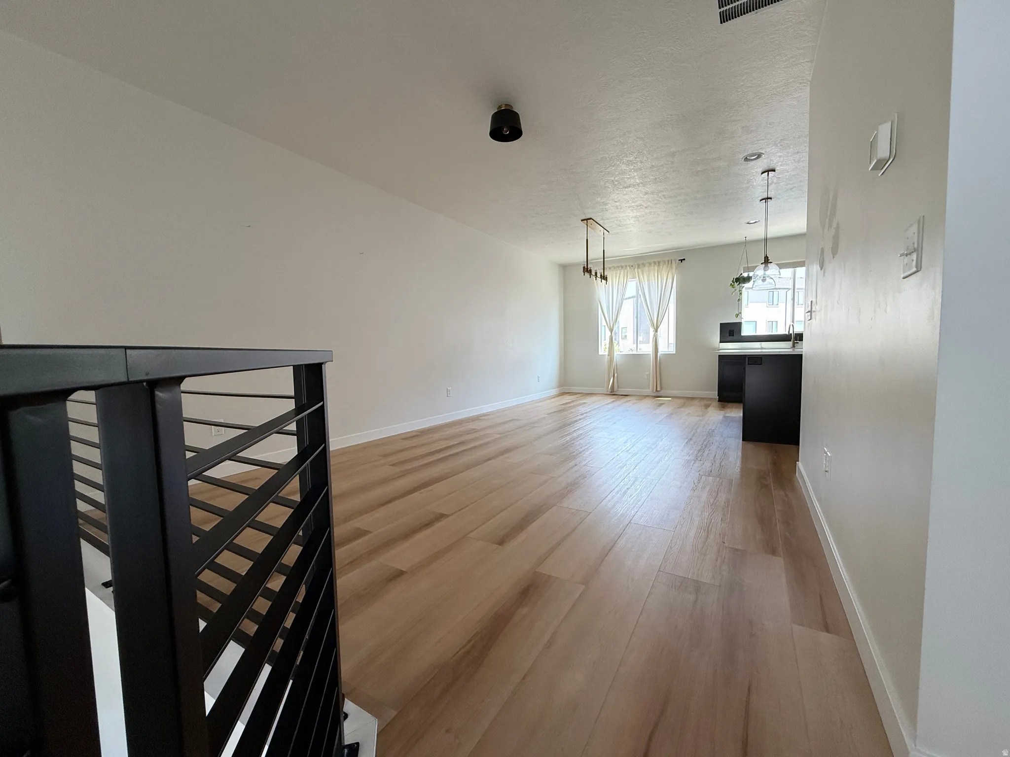 Light wood-finish flooring, white walls, black metal railing, pendant lighting, and a kitchen island with dark cabinetry