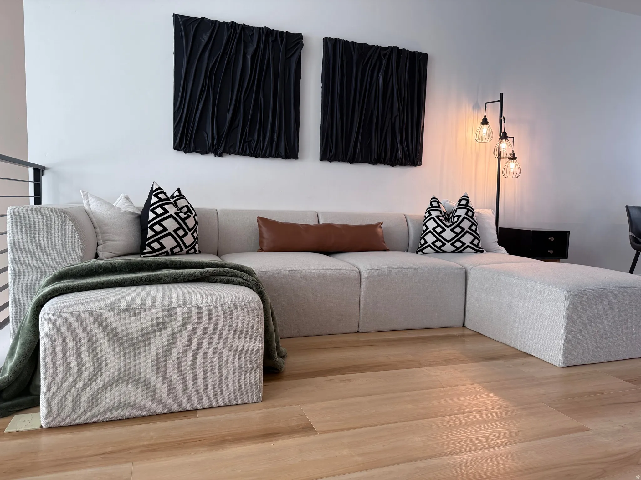 Spacious open-concept area featuring light wood-finish flooring, a contemporary industrial-style floor lamp, and a modern metal railing