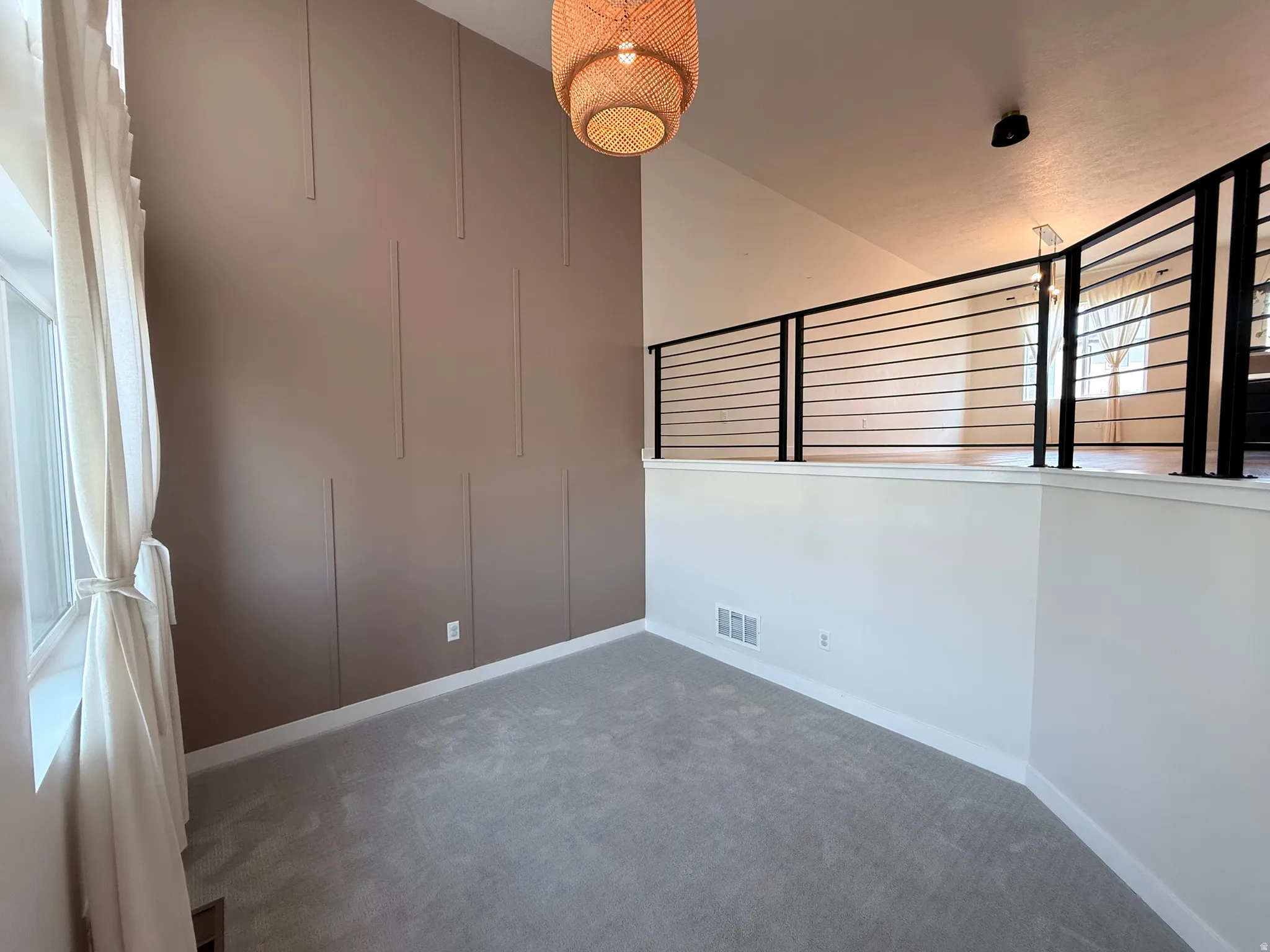 Loft area featuring a contemporary railing, high ceilings, decorative wall paneling, and a unique woven light fixture