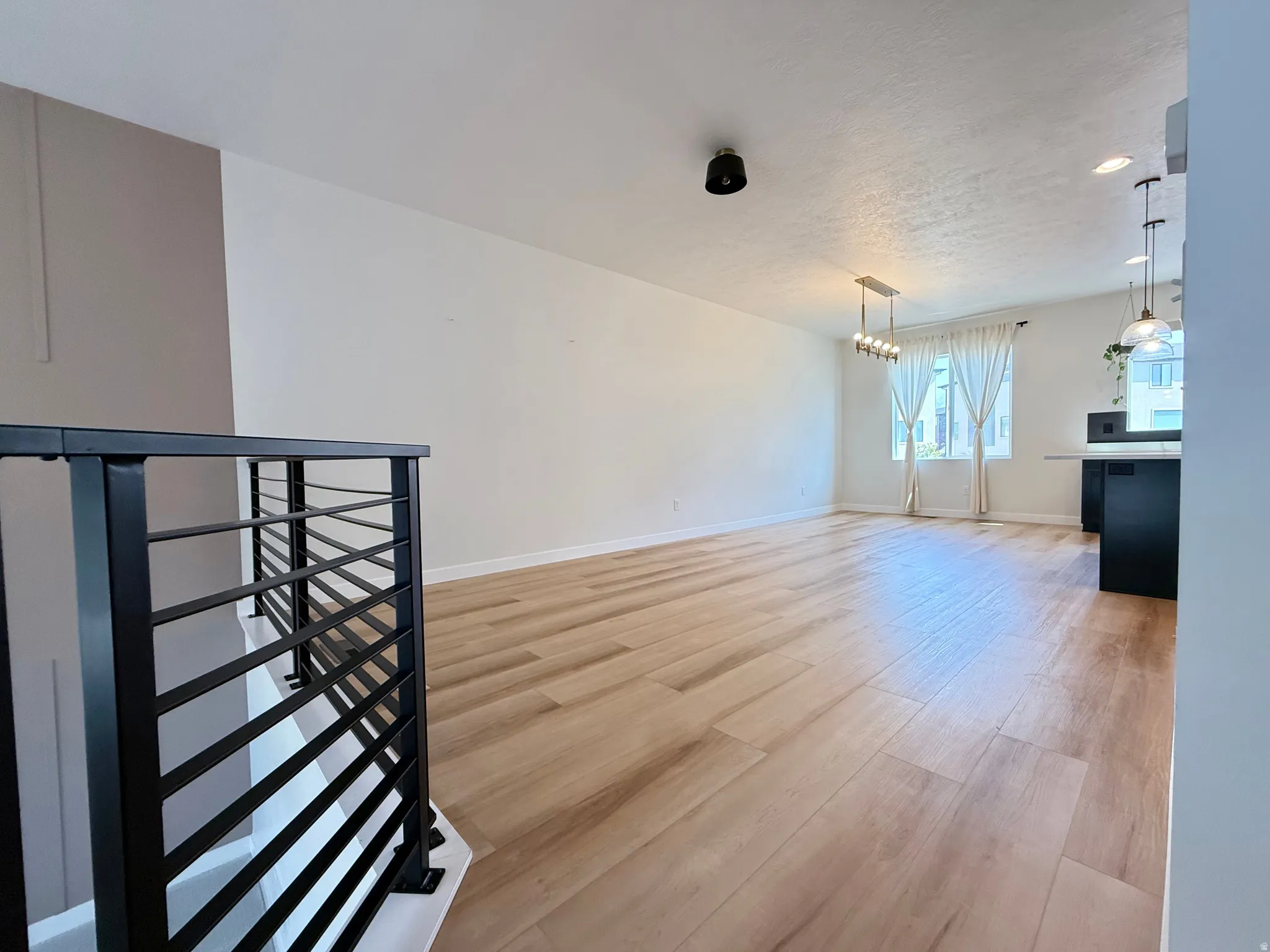 Wood-finish flooring throughout, modern black metal railing, recessed lighting, and contemporary pendant fixtures