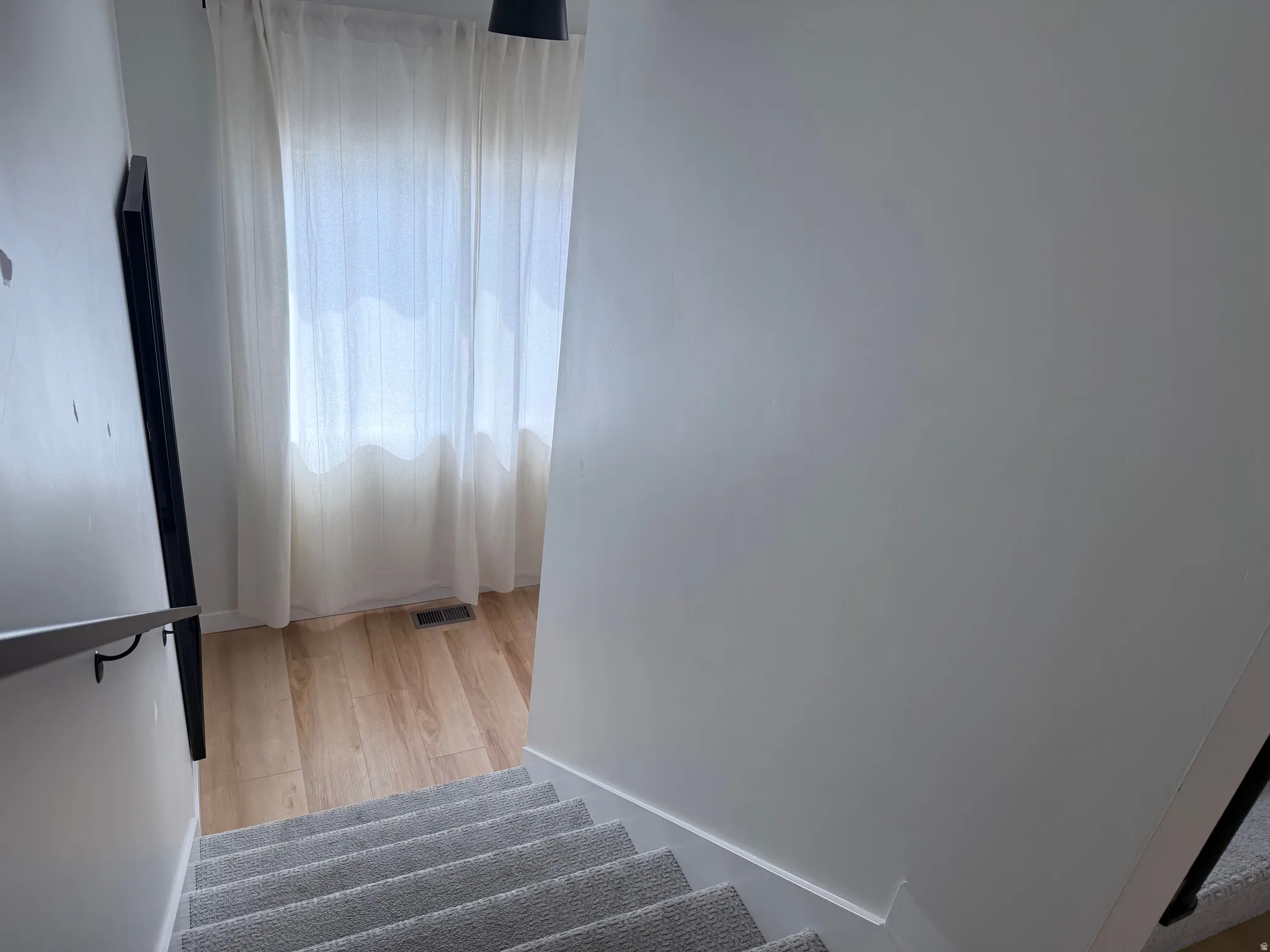 Carpeted staircase with a contemporary metal handrail and light-toned wood-finish flooring