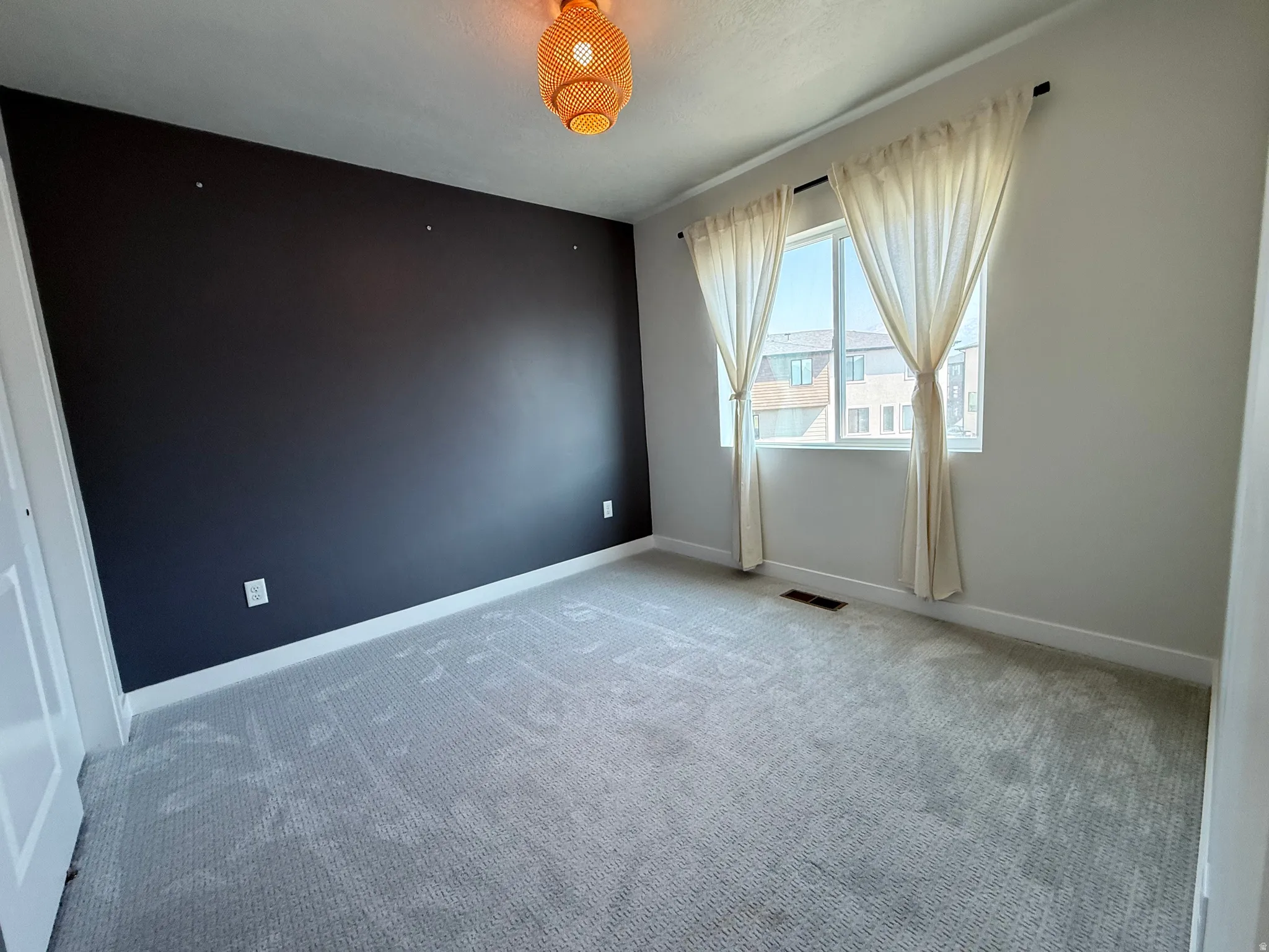 Carpeted room with a dark accent wall, white trim, and a window