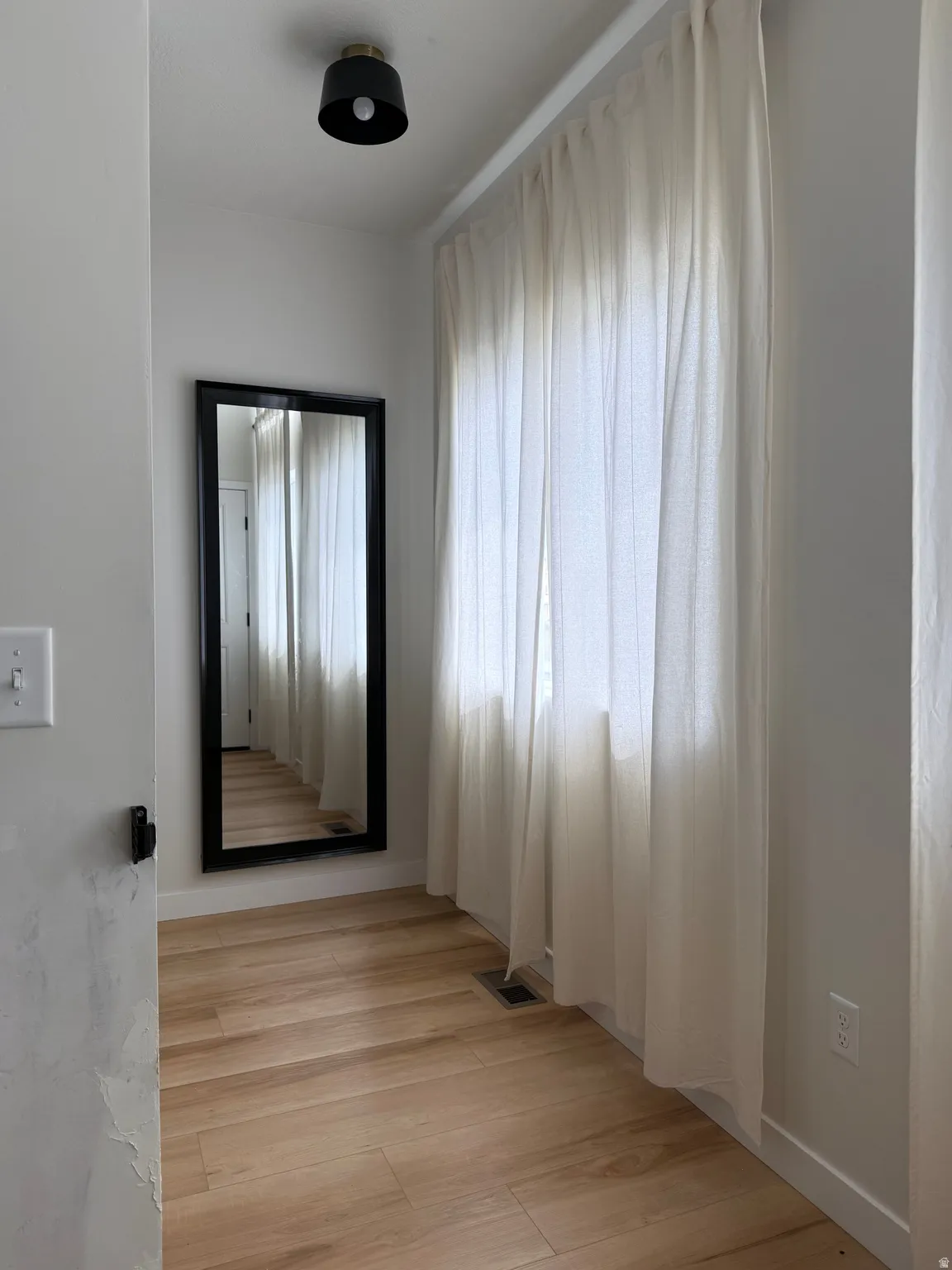Room featuring wood-finish flooring, a contemporary flush-mount light fixture, and a full-length wall mirror