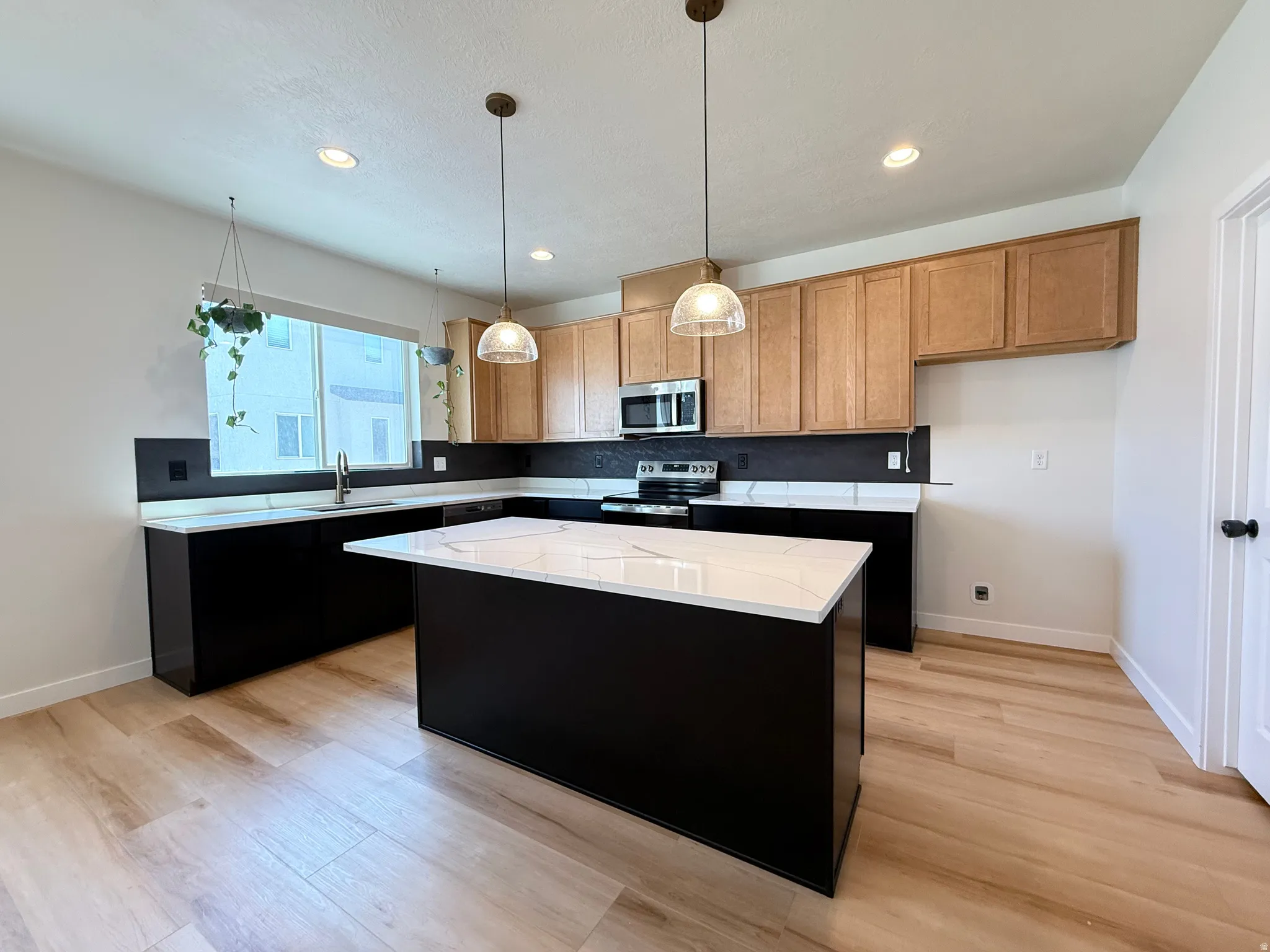 Kitchen featuring wood-finish flooring, two-tone cabinetry, stainless steel appliances, a center island with a white countertop, and recessed lighting