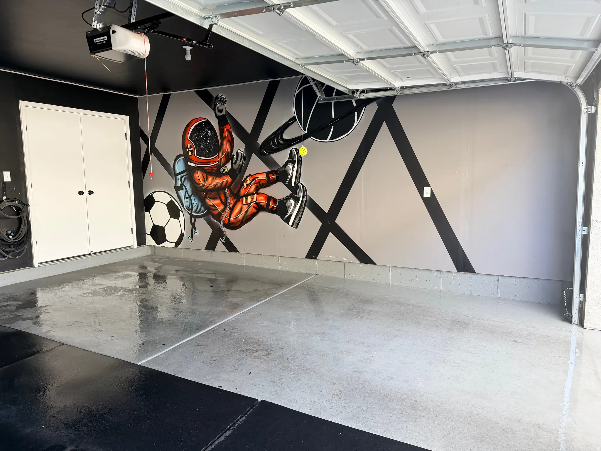 Garage space featuring epoxy flooring, a decorative wall mural, and dual white storage doors