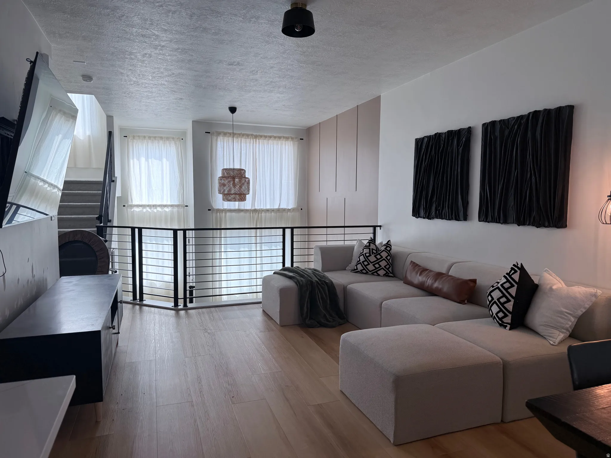 Open-concept living space featuring light wood-finish flooring, a contemporary black metal railing, and white wall paneling
