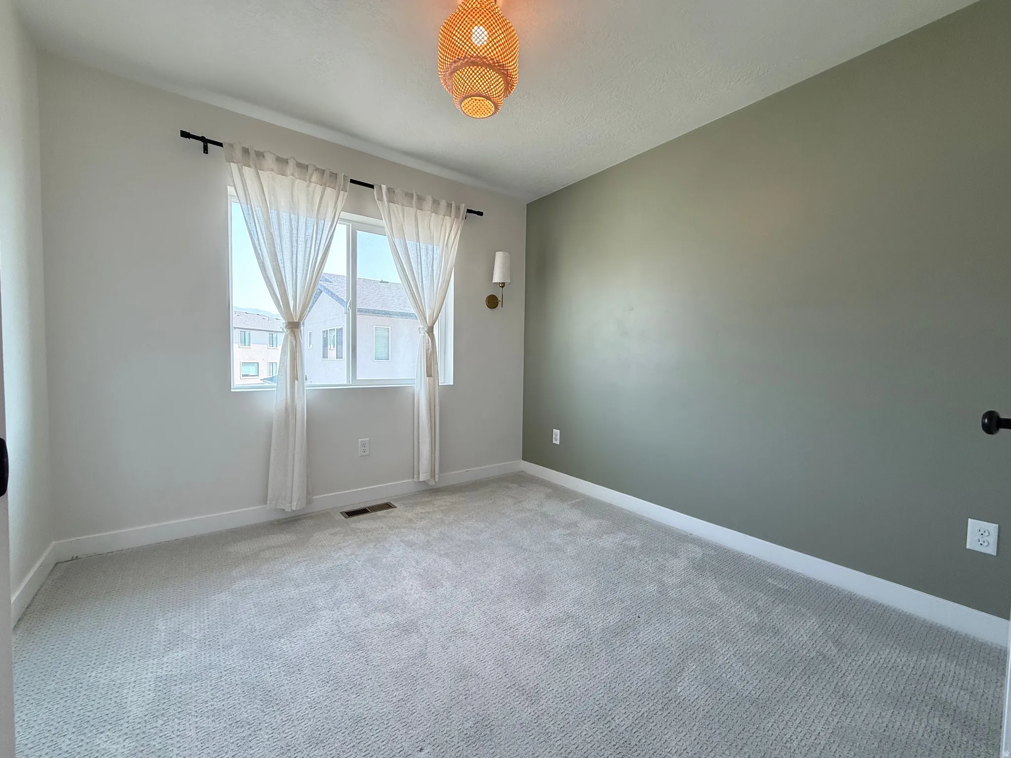 Carpeted flooring with white baseboards, a single window, and a light fixture with a woven shade