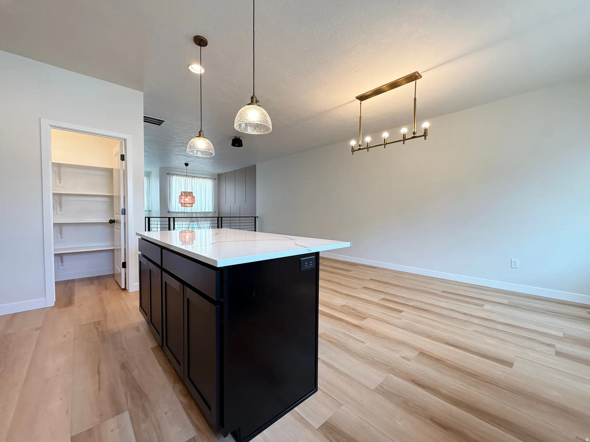Kitchen island with dark cabinetry and a light-toned countertop, accompanied by two pendant lights and a linear chandelier