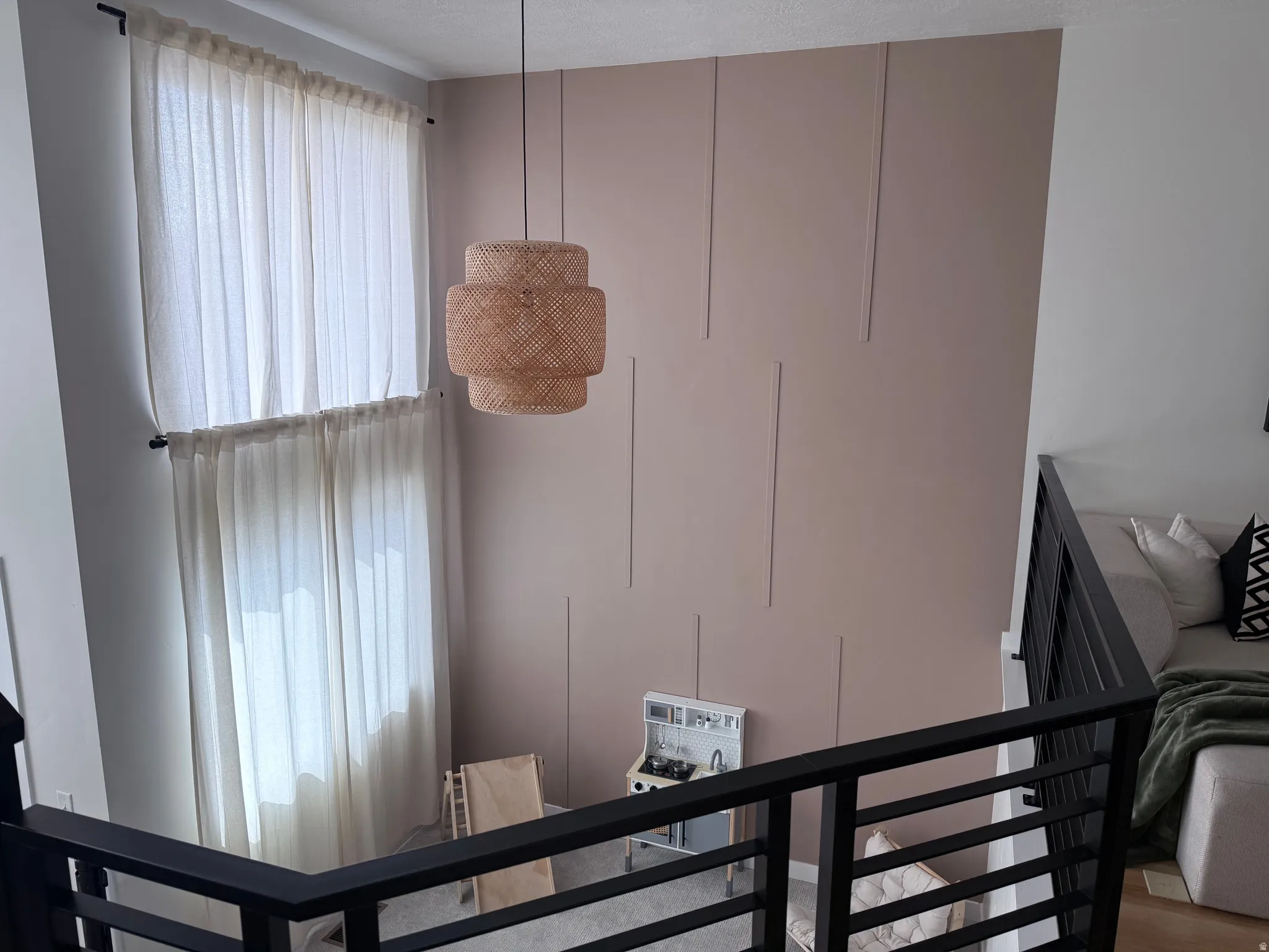 Two-story room featuring a decorative accent wall with vertical paneling, a large suspended light fixture, and a black metal railing